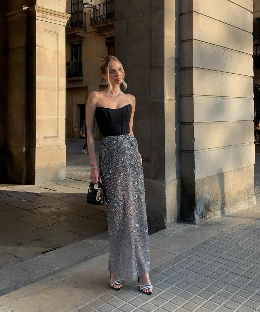 Elegante mulher à luz do sol usa vestido longo formal com corpete preto e saia brilhante prateada.