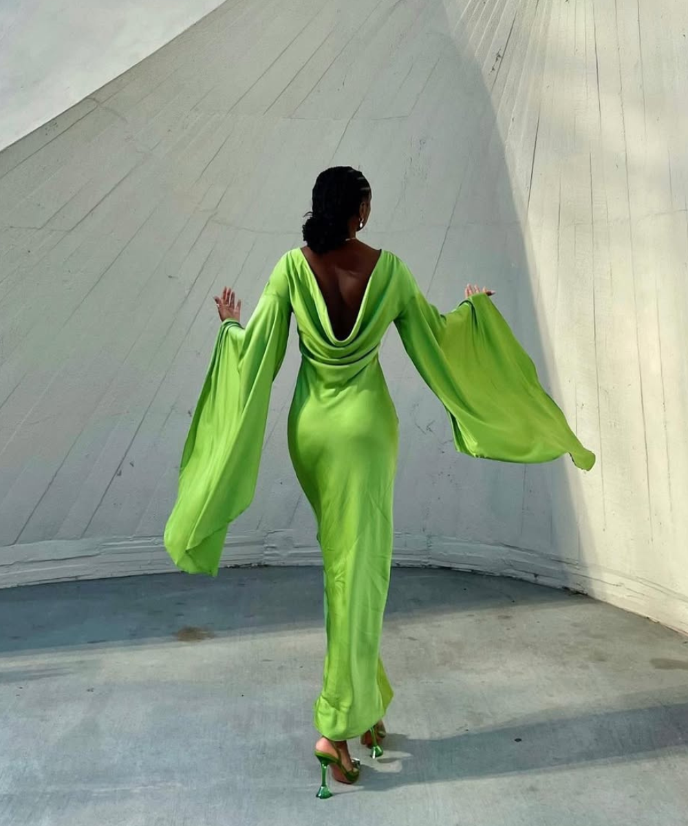 Pessoa vestindo traje longo verde neão com mangas largas, capturada de costas.