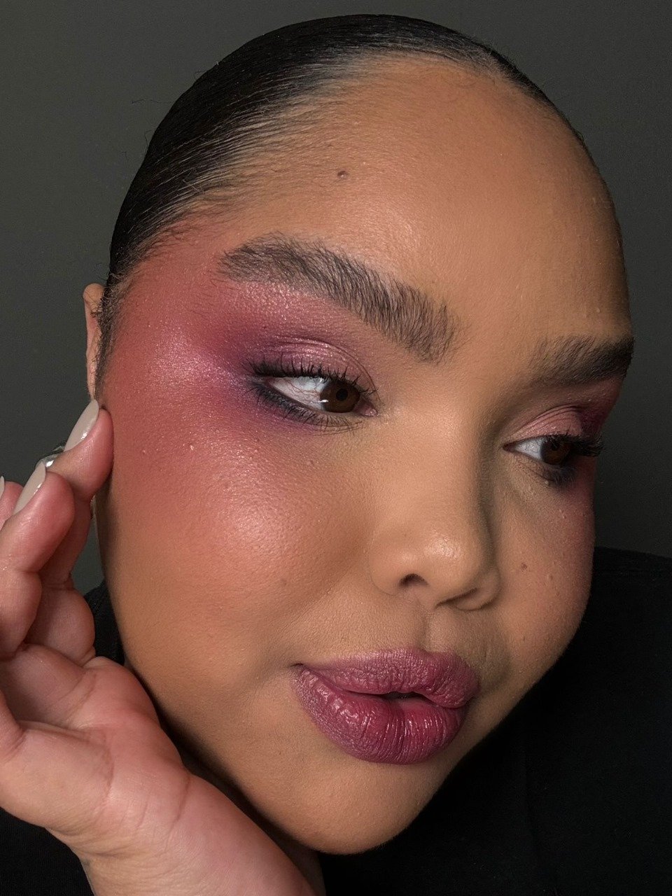 Maquiagem em tons de rosa com sombra e batom roxo suave, realçando a beleza da pele.