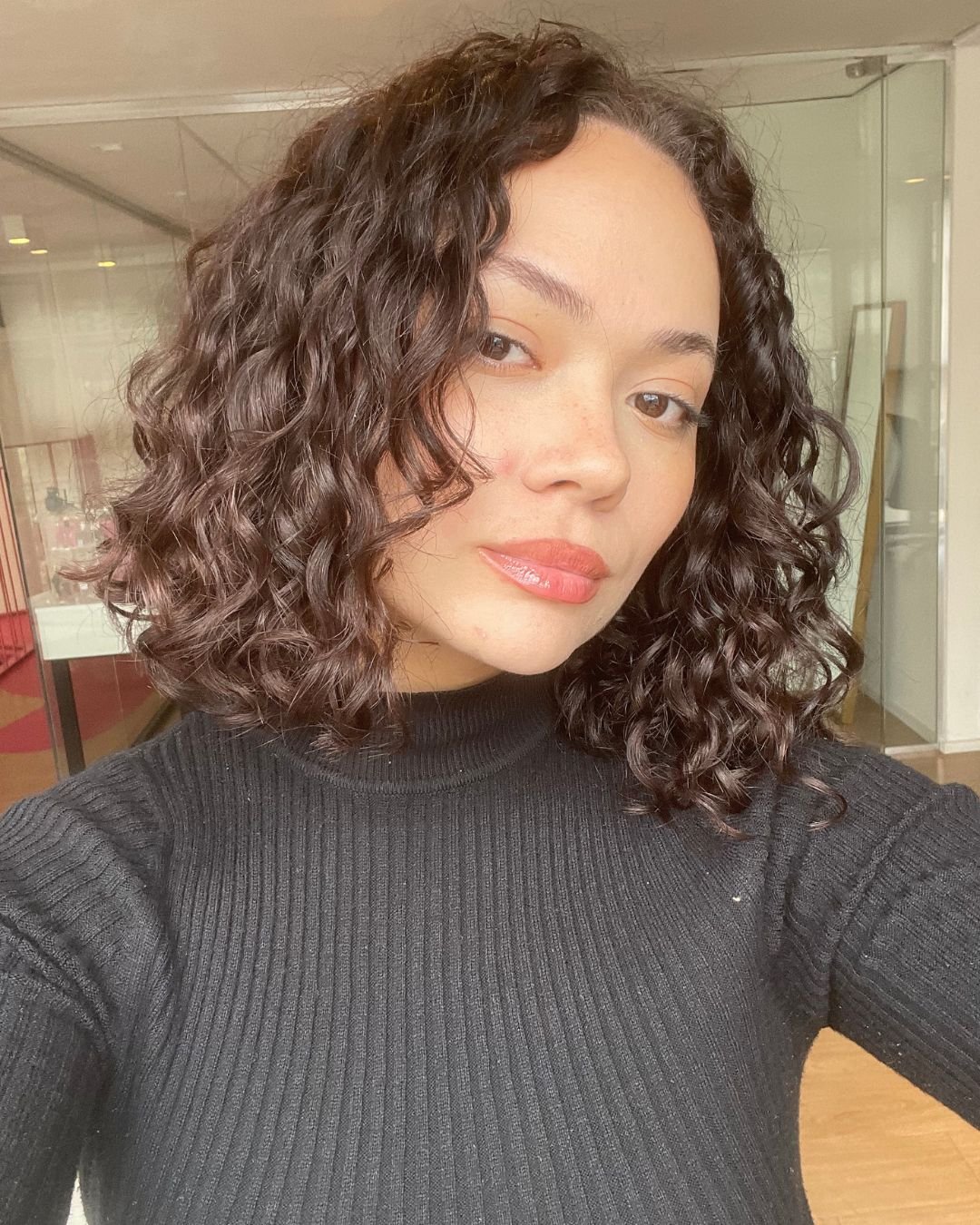stefany de blusa preta depois de usar a linha para cabelos cacheados