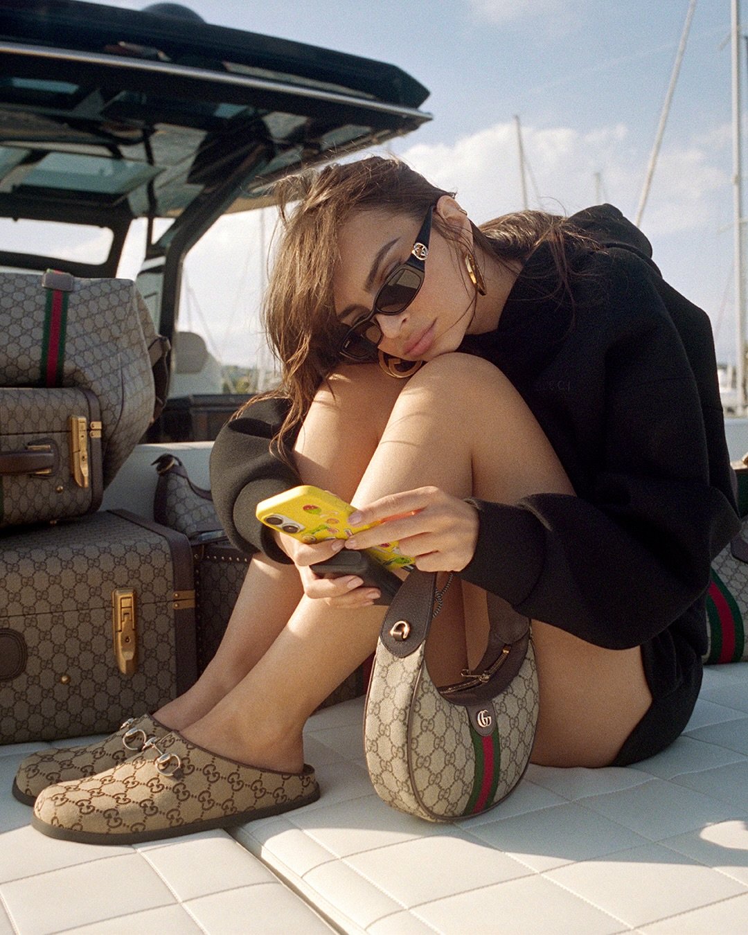 Mulher no barco com acessórios GG Monogram, usando óculos escuros e celular.