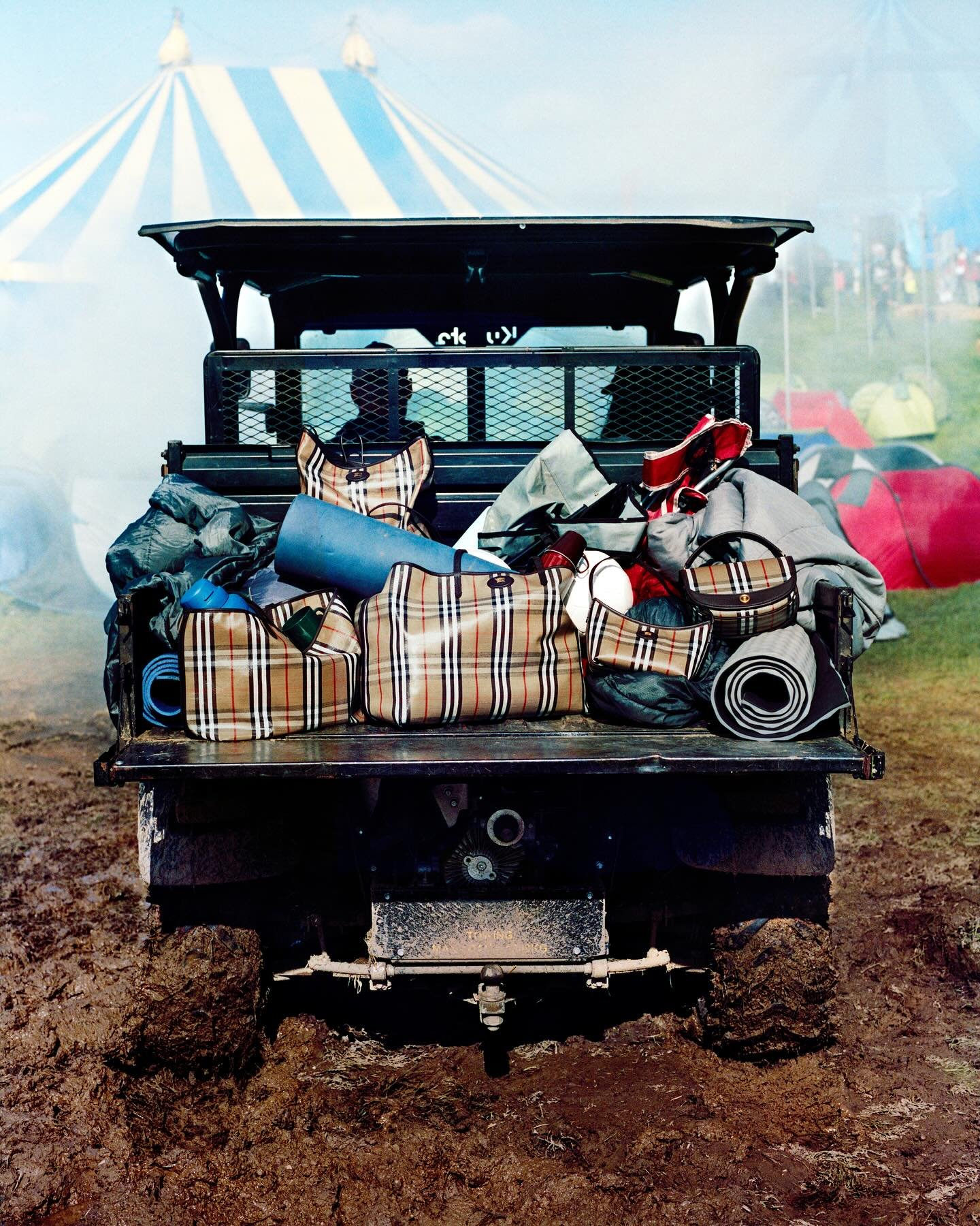 Veículo com malas xadrez Burberry na lama. Ao fundo, tenda listrada em um dos Festivais Burberry