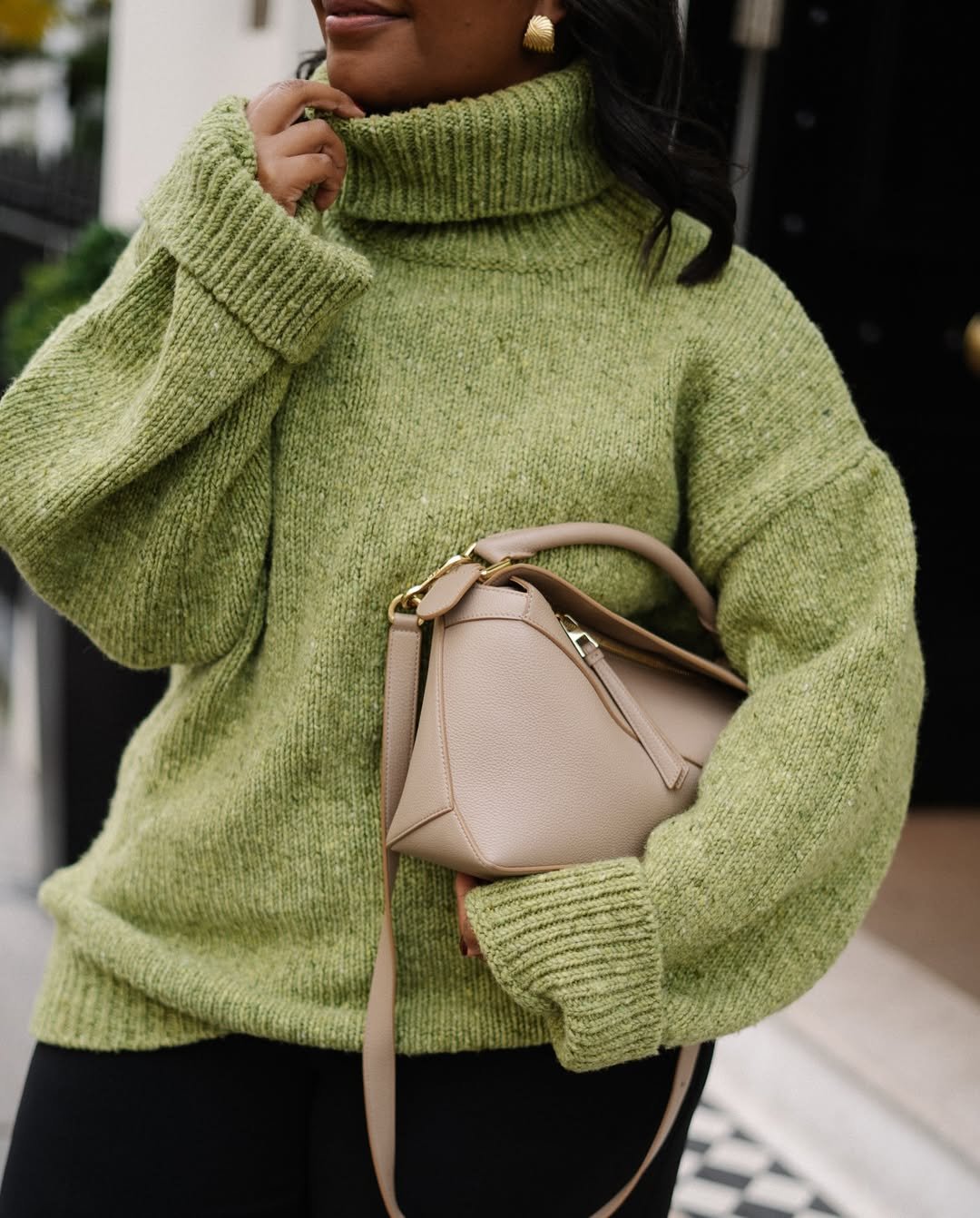 Suéter verde volumoso com gola alta, bolsa bege e brinco dourado como acessórios.