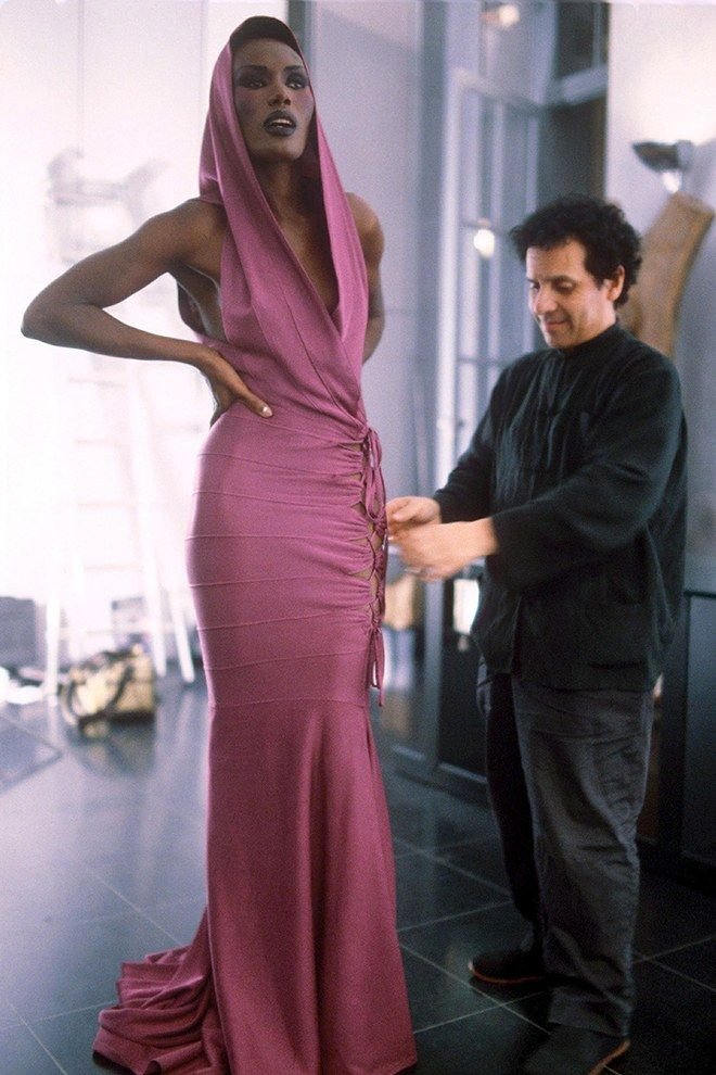 Pessoa ajustando vestido Alaïa roxo elegante em modelo, com capuz e detalhes frontais.