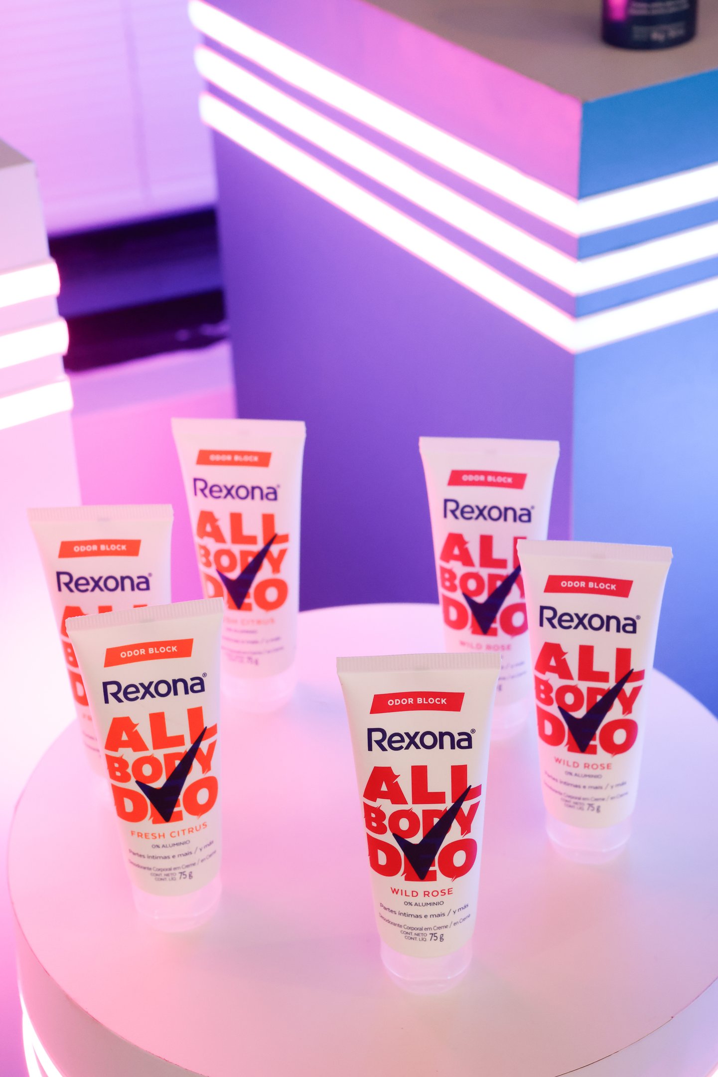 Tubos do All Body Deo Rexona em uma mesa sob luz rosa, destacando as opções Fresh Citrus e Wild Rose.