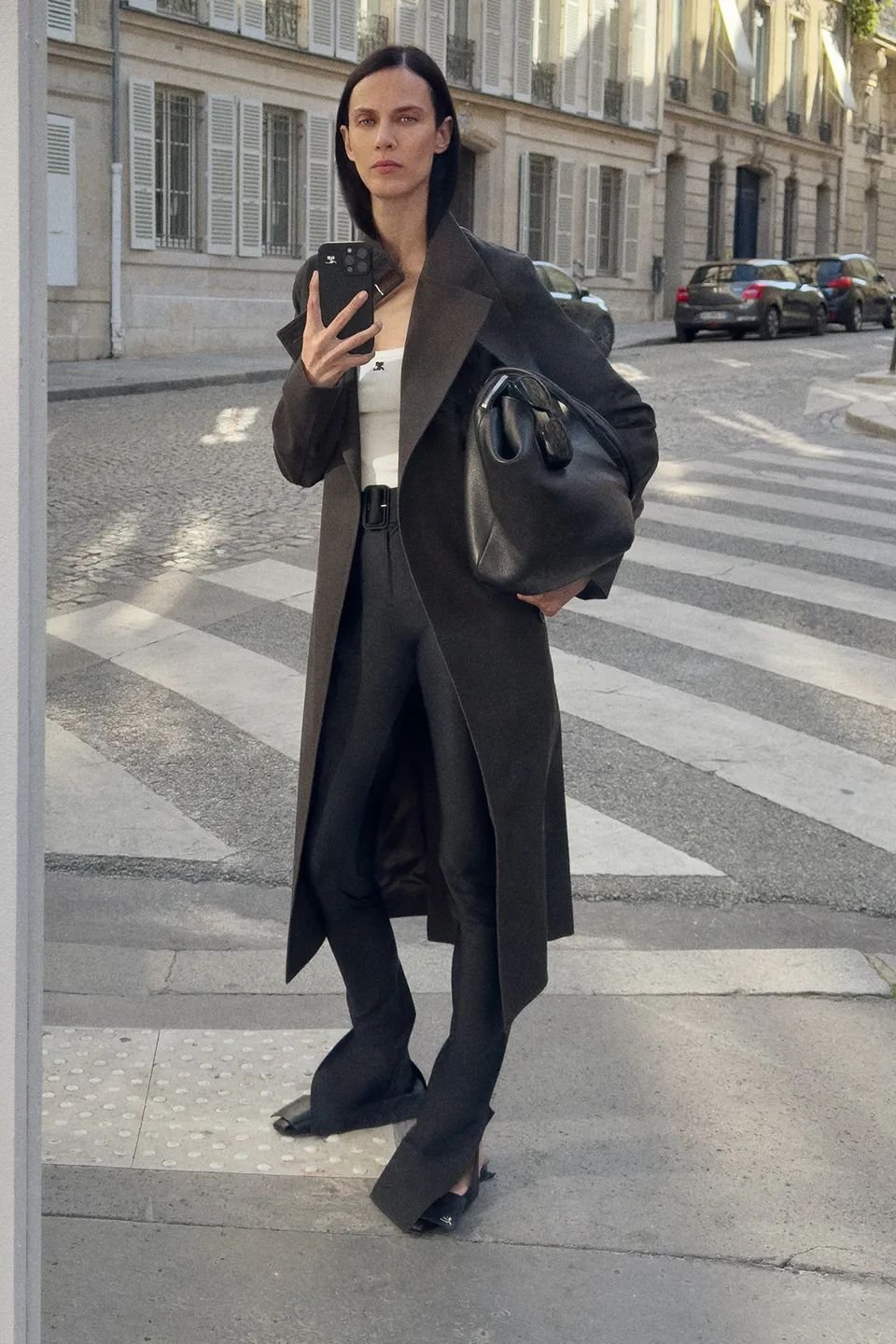 Pessoa com casaco longo escuro, segurando bolsa preta, em uma rua urbana. Não é possível integrar a palavra-chave.
