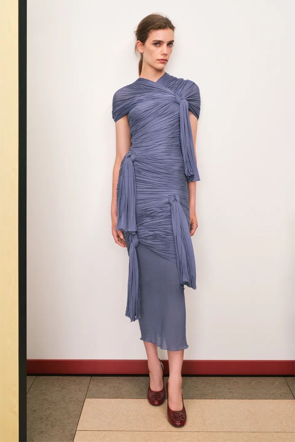 Vestido azul drapeado, estilo bandage, com sapatos vermelhos.