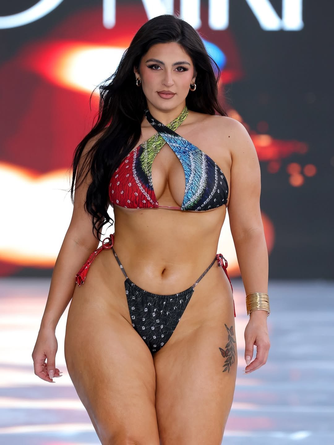 Modelo desfila com biquíni colorido, destacando tendências de biquíni, em uma passarela iluminada.