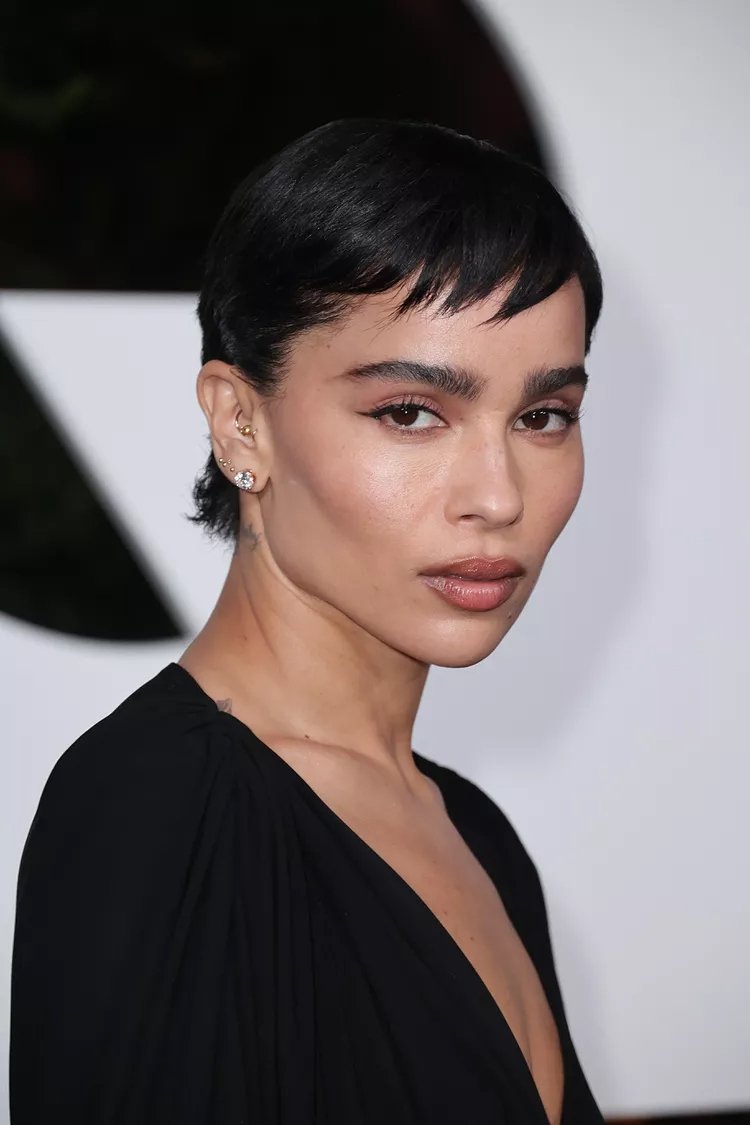 Pessoa com cabelo estilo bixie cut curto e escuro, usando brincos e vestido preto.