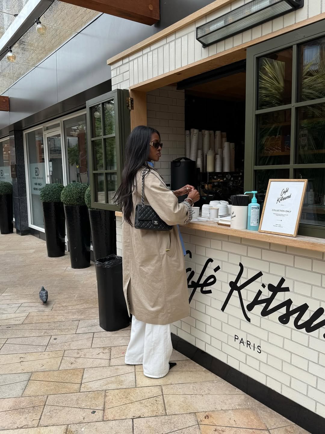 Pessoa com bolsa matelassê em frente ao Café Kitsuné, vestindo casaco bege e calça branca.