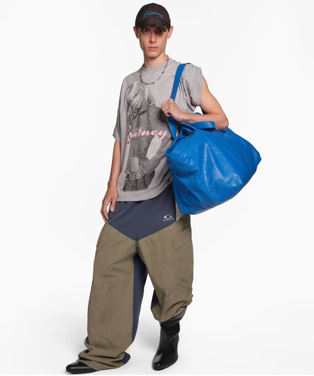 Modelo vestindo camiseta com imagem de Britney Spears, boné combinando, calças largas Balenciaga e bolsa azul.