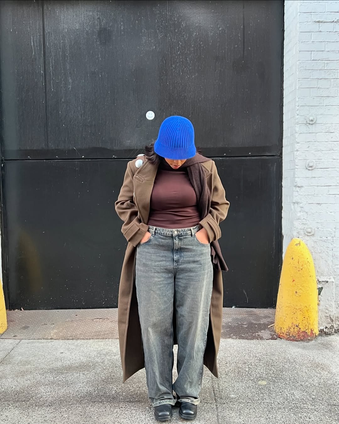 Pessoa com chapéu azul e sobretudo marrom veste calça jeans de corte largo, destacando o estilo casual de 2025.