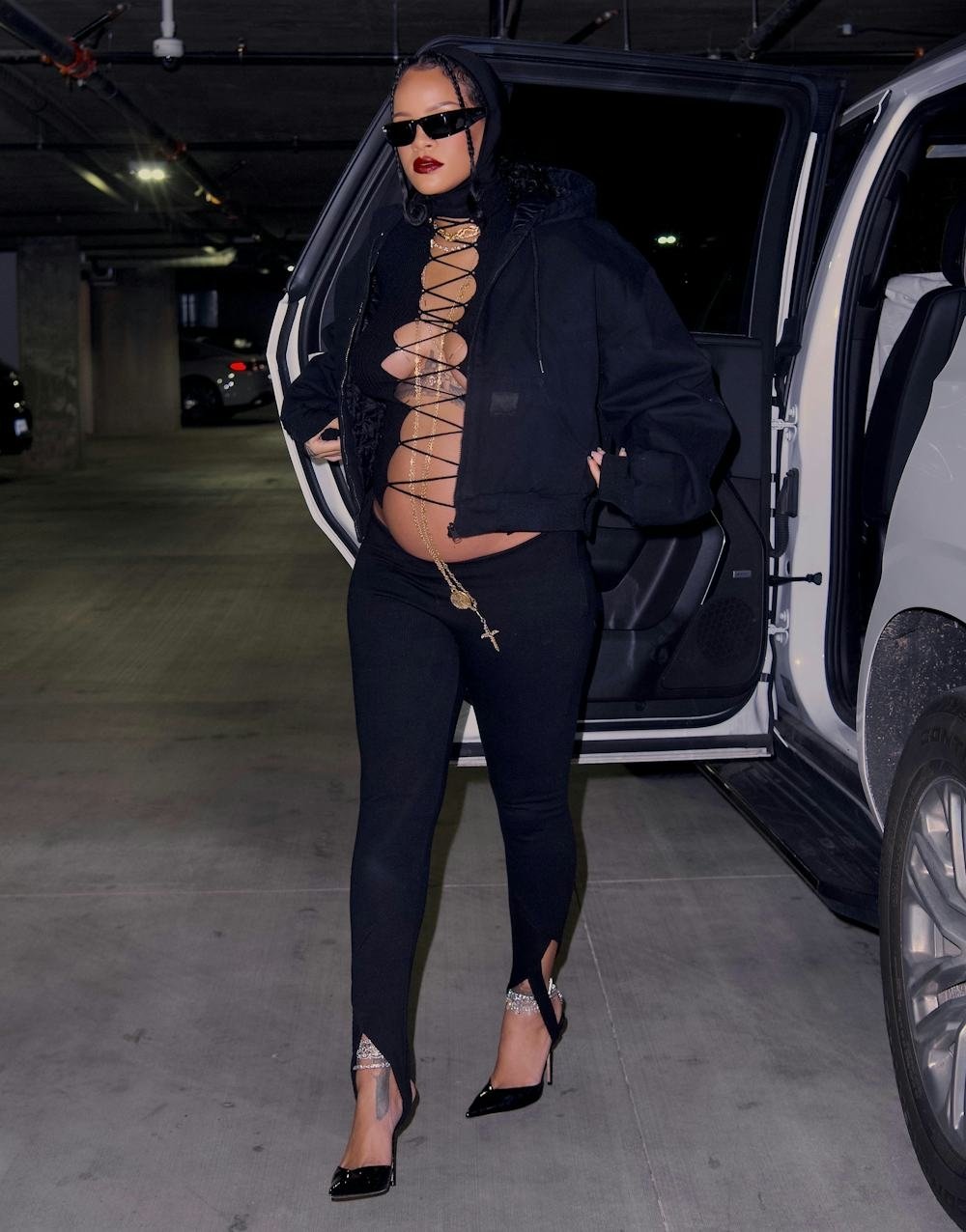 Mulher grávida usando legging fusô preta e casaco, saindo de um carro em garagem.