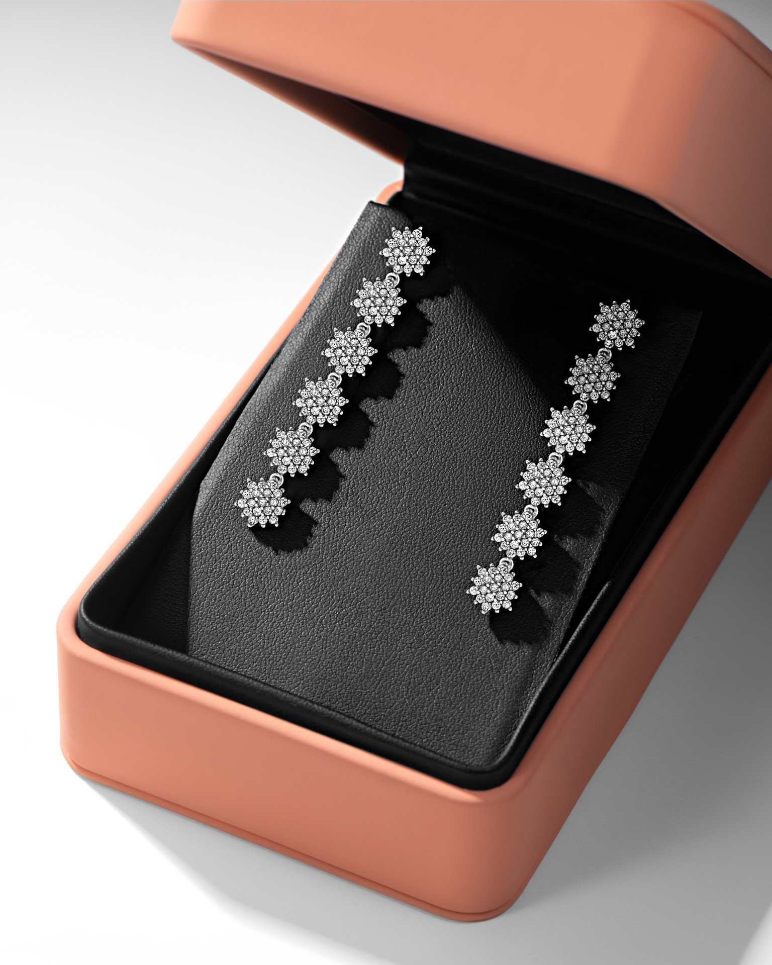 Estojo rosa aberto exibe um par de brincos de diamante em formato de flor sobre base preta.