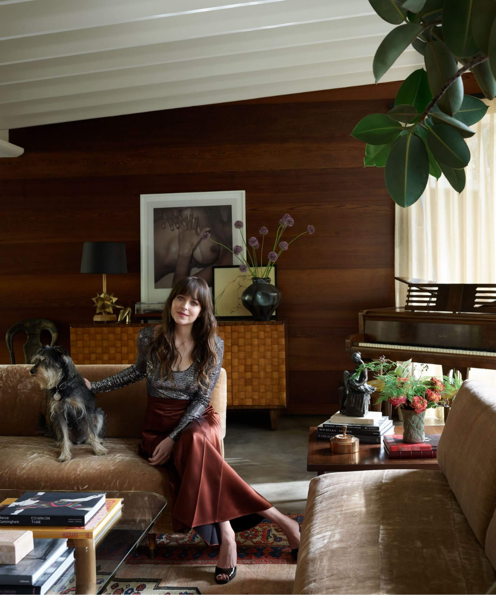 Sala de estar elegante com mulher sentada em sofá ao lado de um cachorro, decoração sofisticada e piano ao fundo.