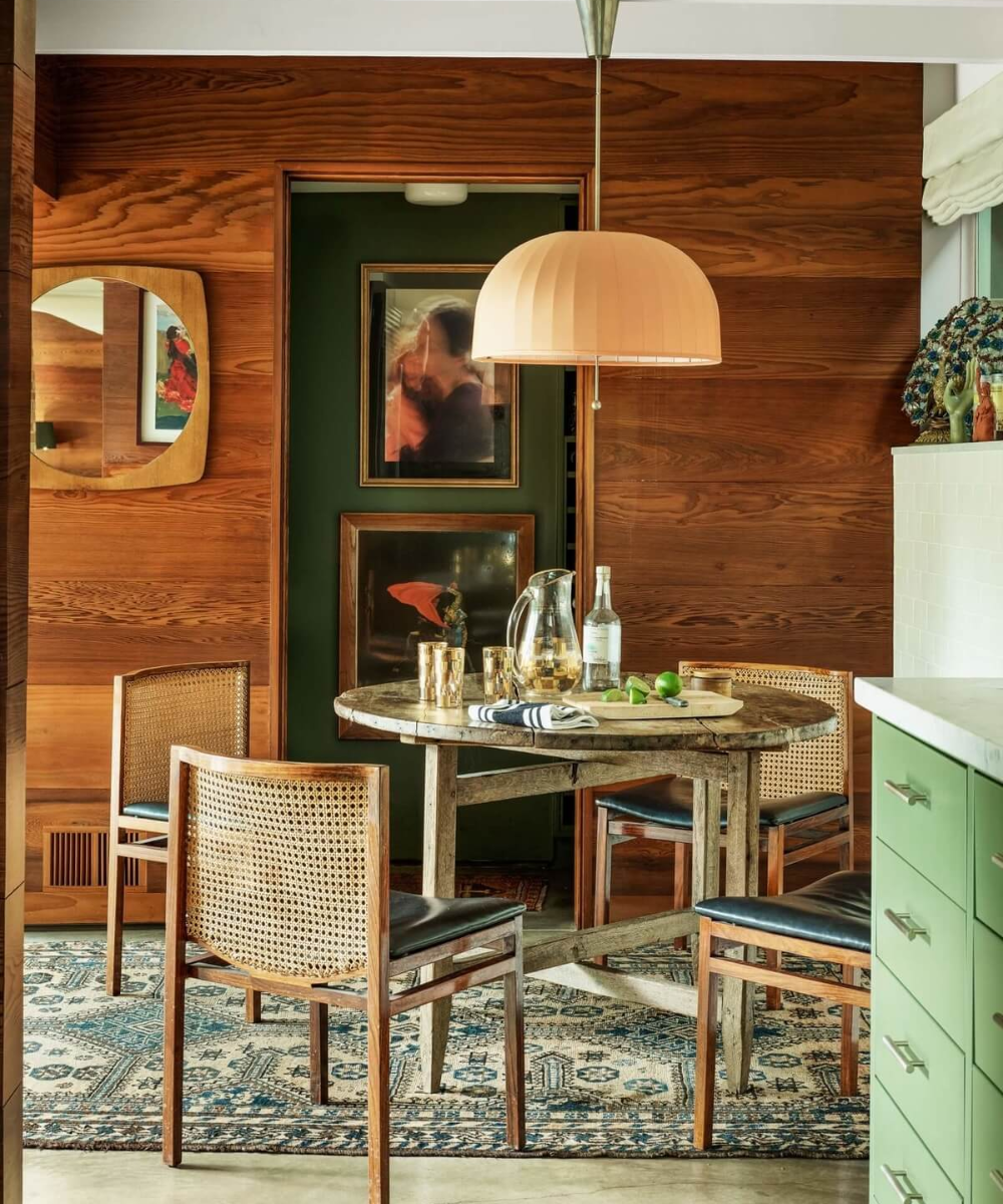 Sala de jantar com mesa redonda e cadeiras rústicas. Decoração sofisticada e luminária pendente elegante.