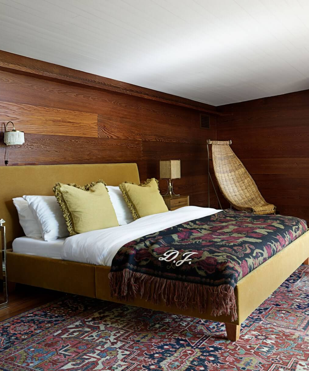 Quarto aconchegante com cama de madeira e manta floral, em espaço com piso e paredes de madeira.