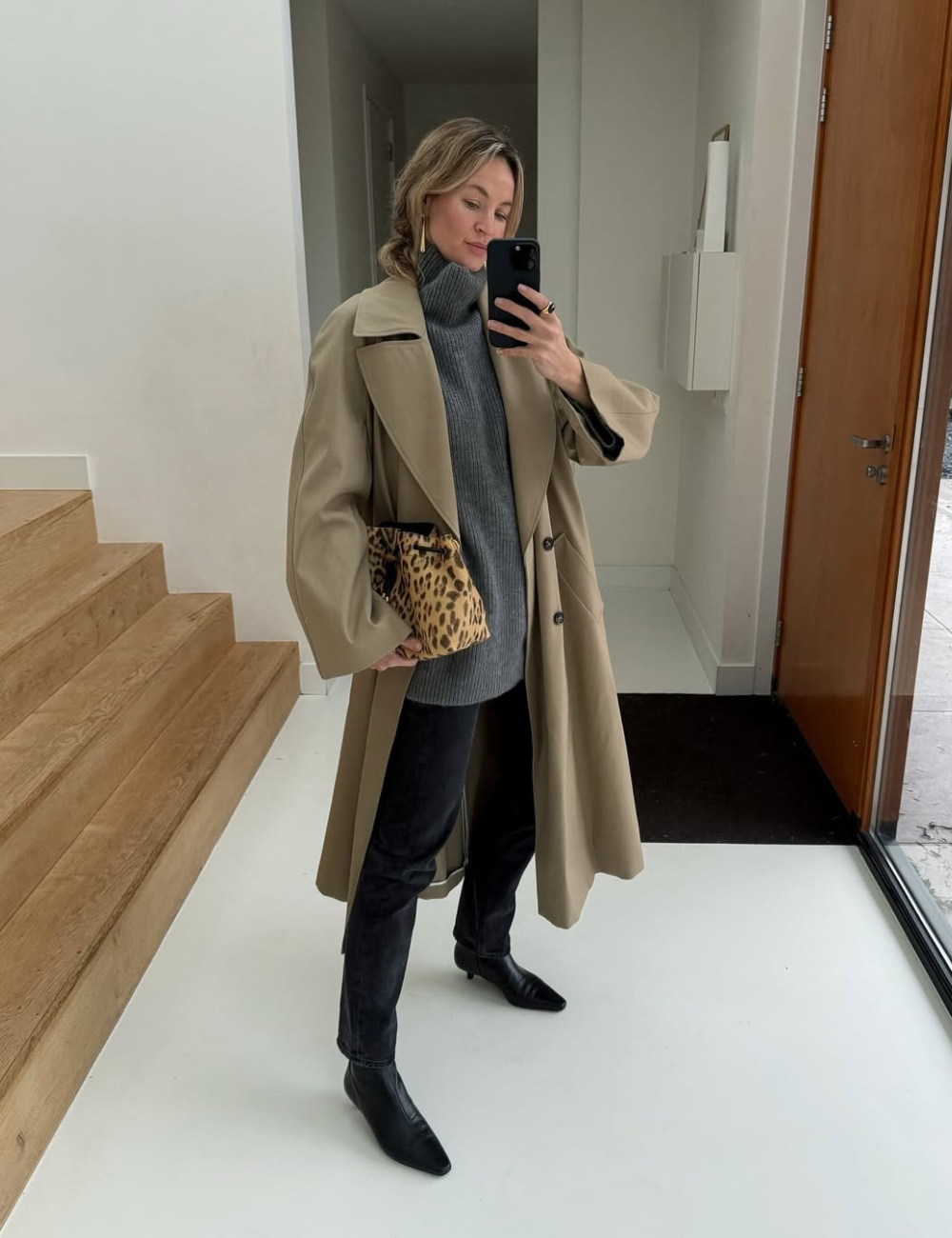 Pessoa vestindo casaco clássico bege, suéter cinza, segurando bolsa de estampa animal.