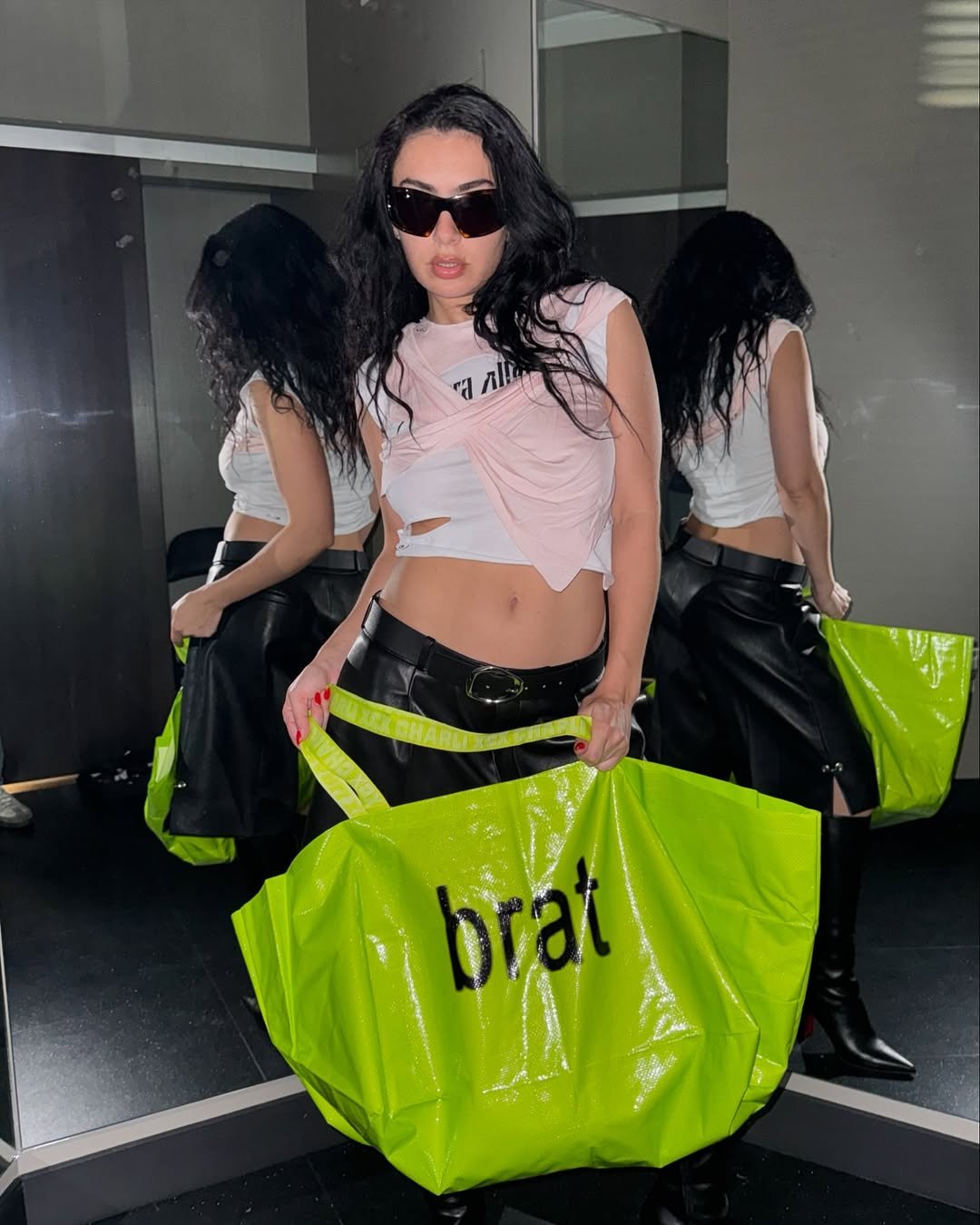 Mulher em frente ao espelho com óculos escuros e bolsa verde em tons neon, refletindo estilo ousado.