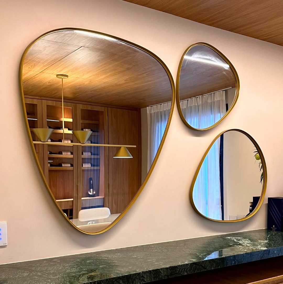 Espelhos decorativos de formatos orgânicos emoldurados em dourado embelezam uma sala pequena e elegante.