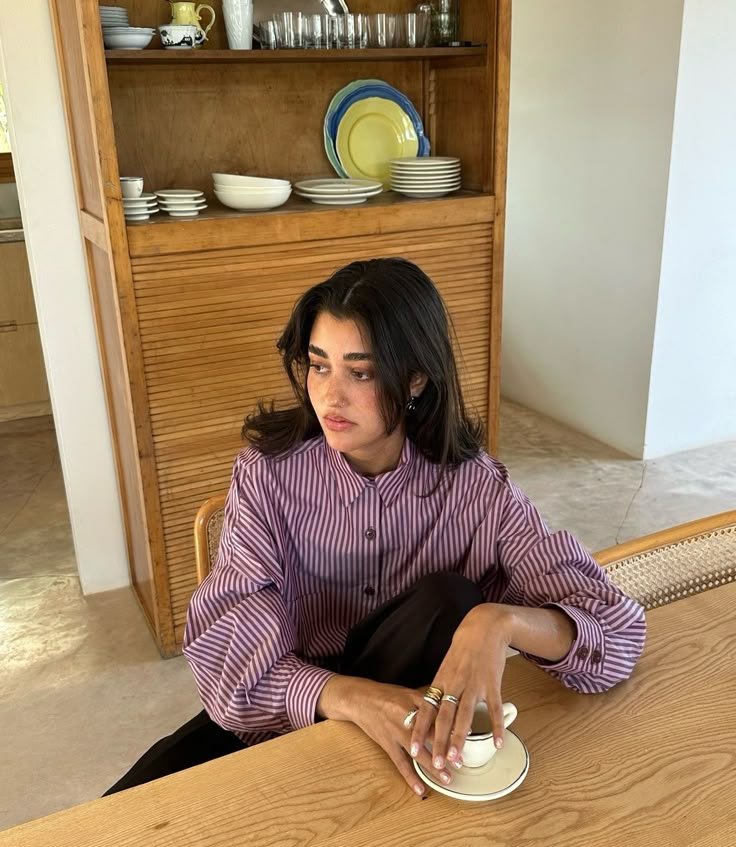 Pessoa pensativa sentada à mesa, em frente a louças coloridas na prateleira. Dias difíceis