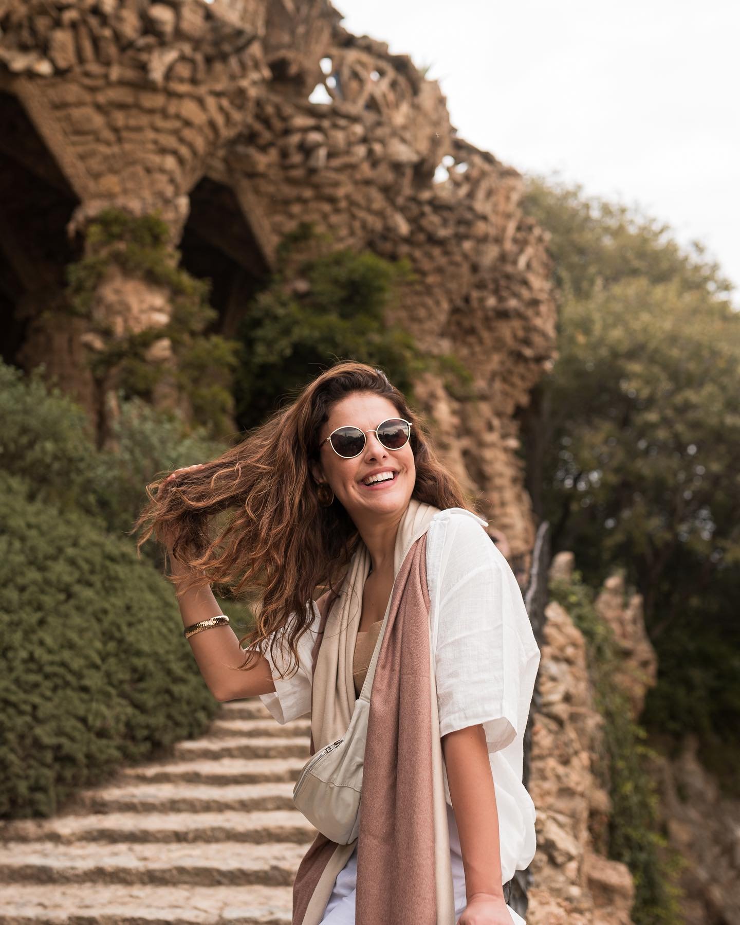 Paloma Bernardi está sorrindo em uma escadaria de pedras, usando óculos escuros e roupa casual.
