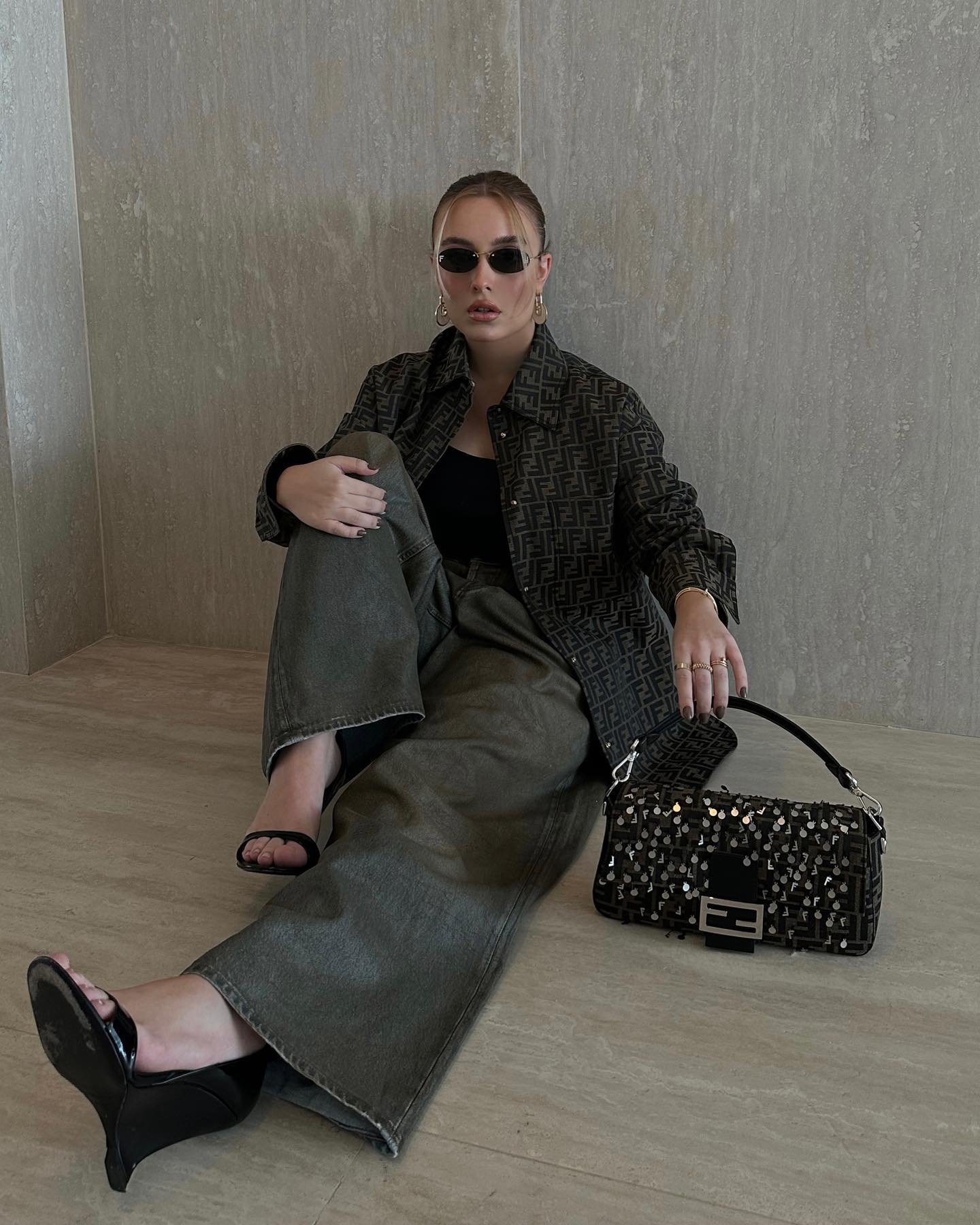 Pessoa com óculos escuros, roupa estampada e bolsa estilosa sentada no chão.