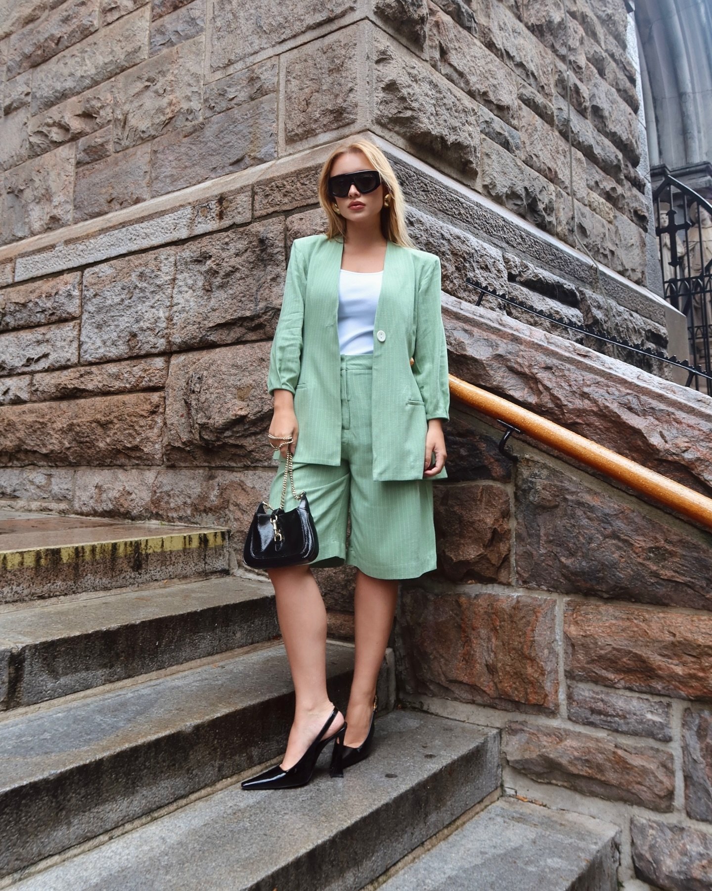 Pessoa de terninho verde claro e sapatos pretos está em uma escada de pedra.