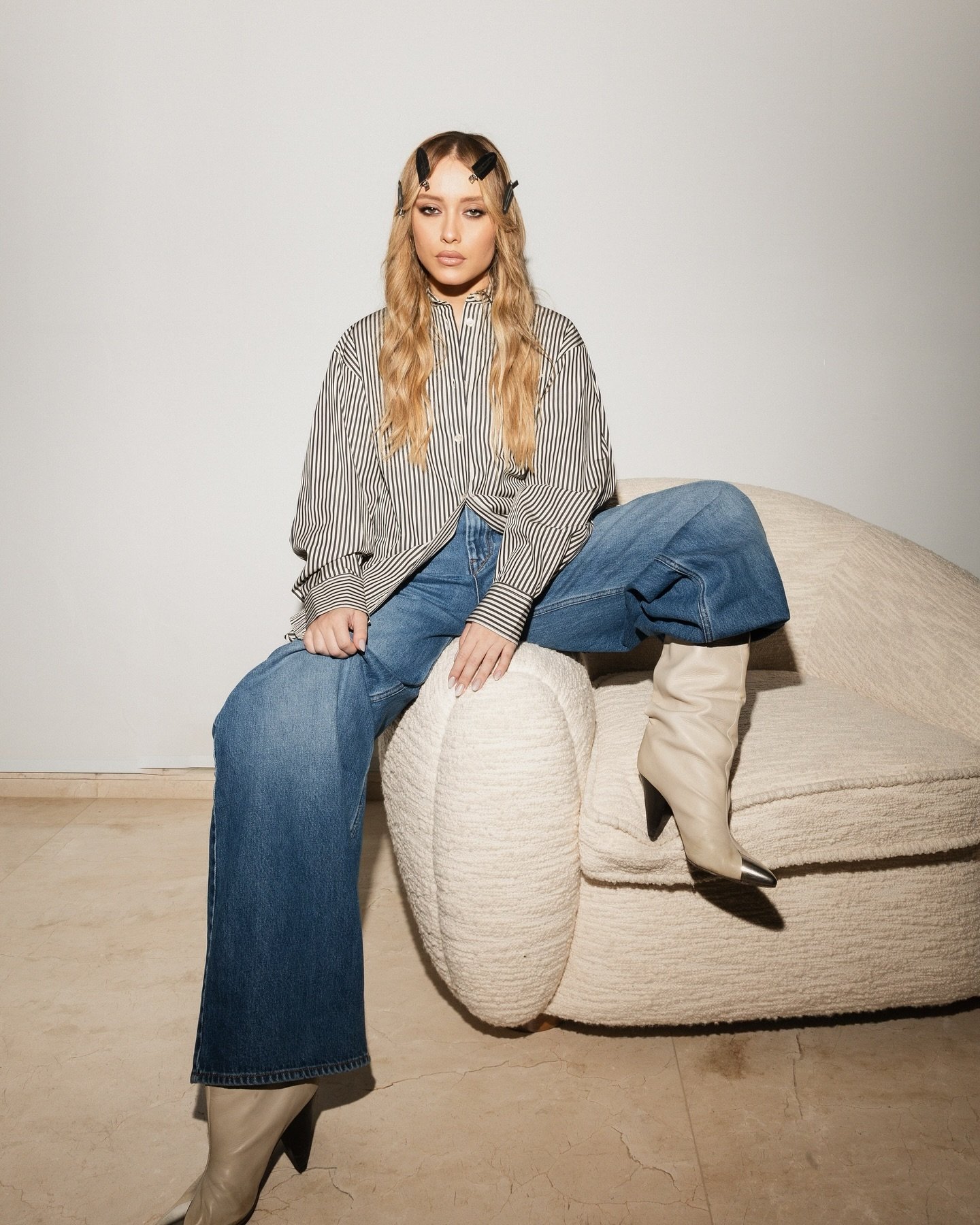 Pessoa vestindo camisa listrada e calça jeans, sentada em um sofá, utilizando botas de couro bege.