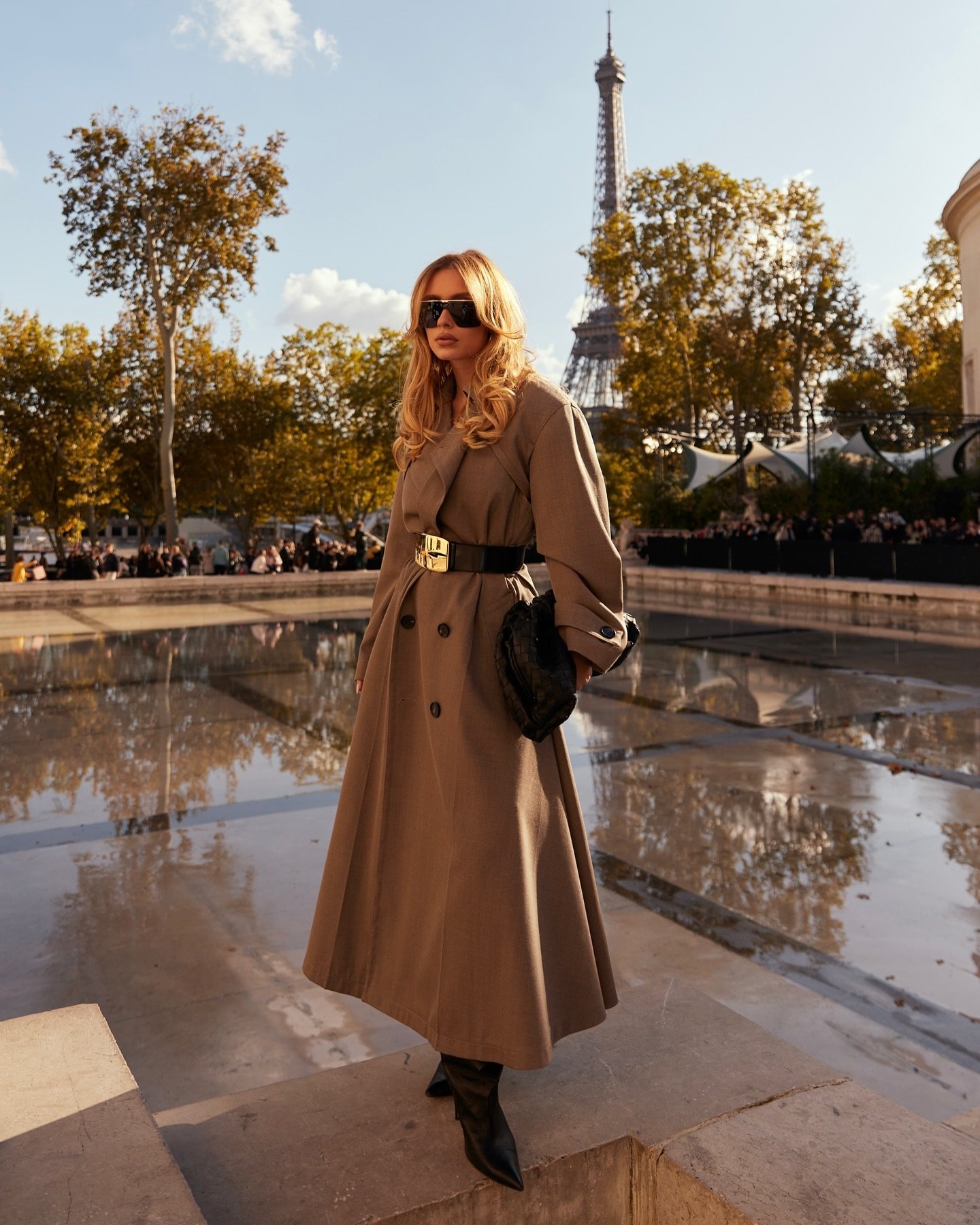 Pessoa elegante de casaco marrom em frente à Torre Eiffel num dia ensolarado, Paris.