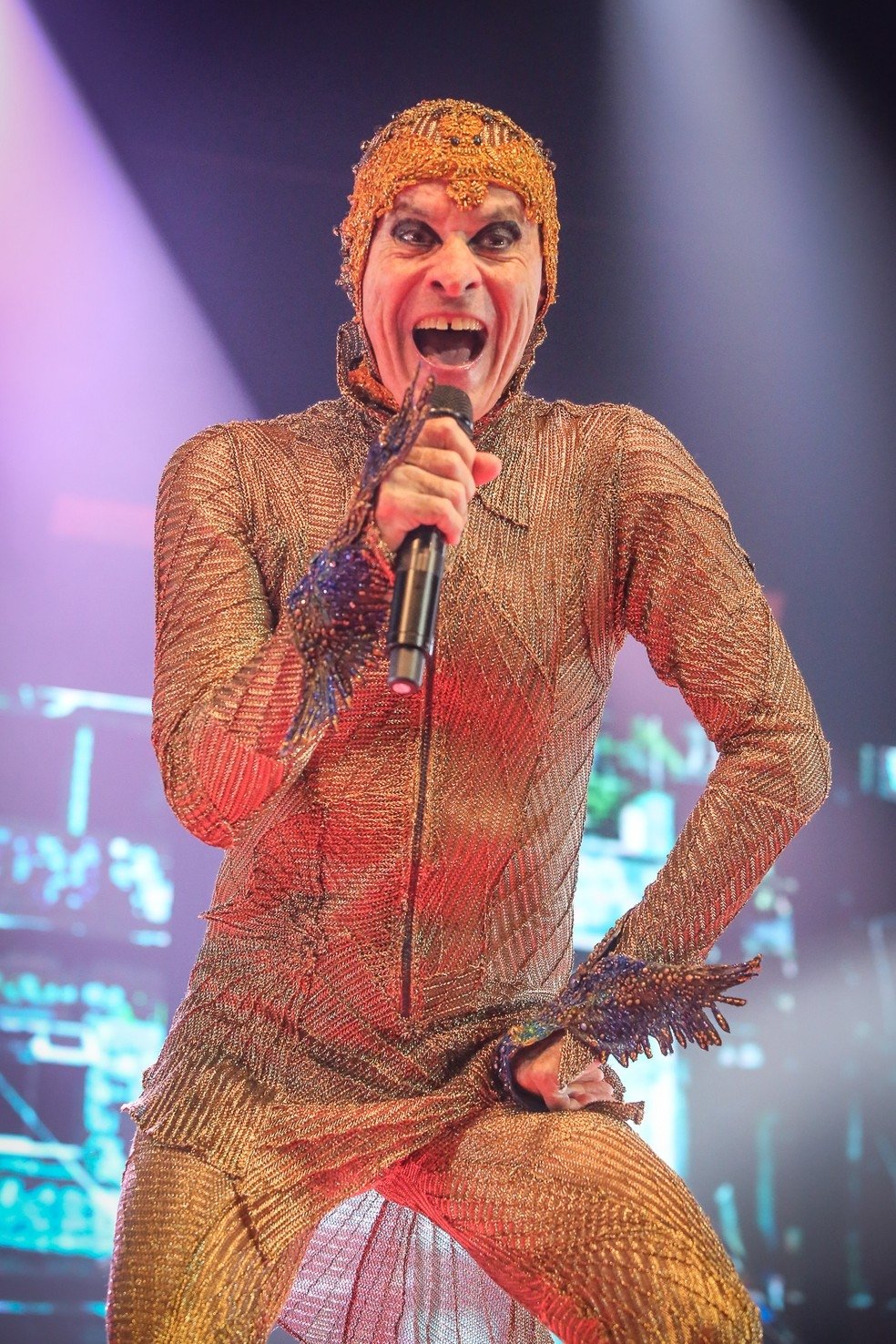 Cantor com figurino extravagante e maquiagem marcante se apresentando em show.