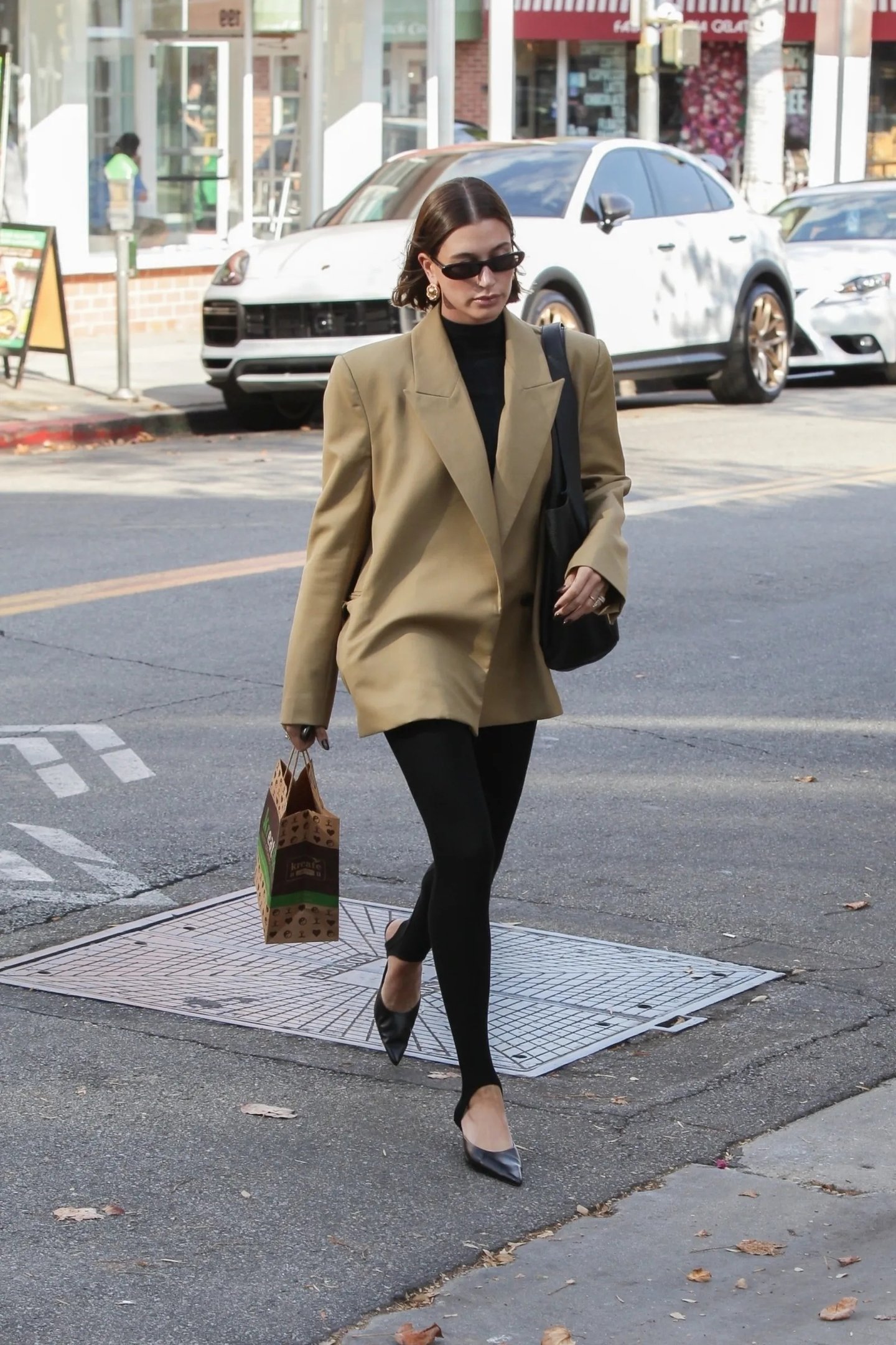 Pessoa usando legging fusô preta e casaco bege, caminhando pela rua com sacola de compras.