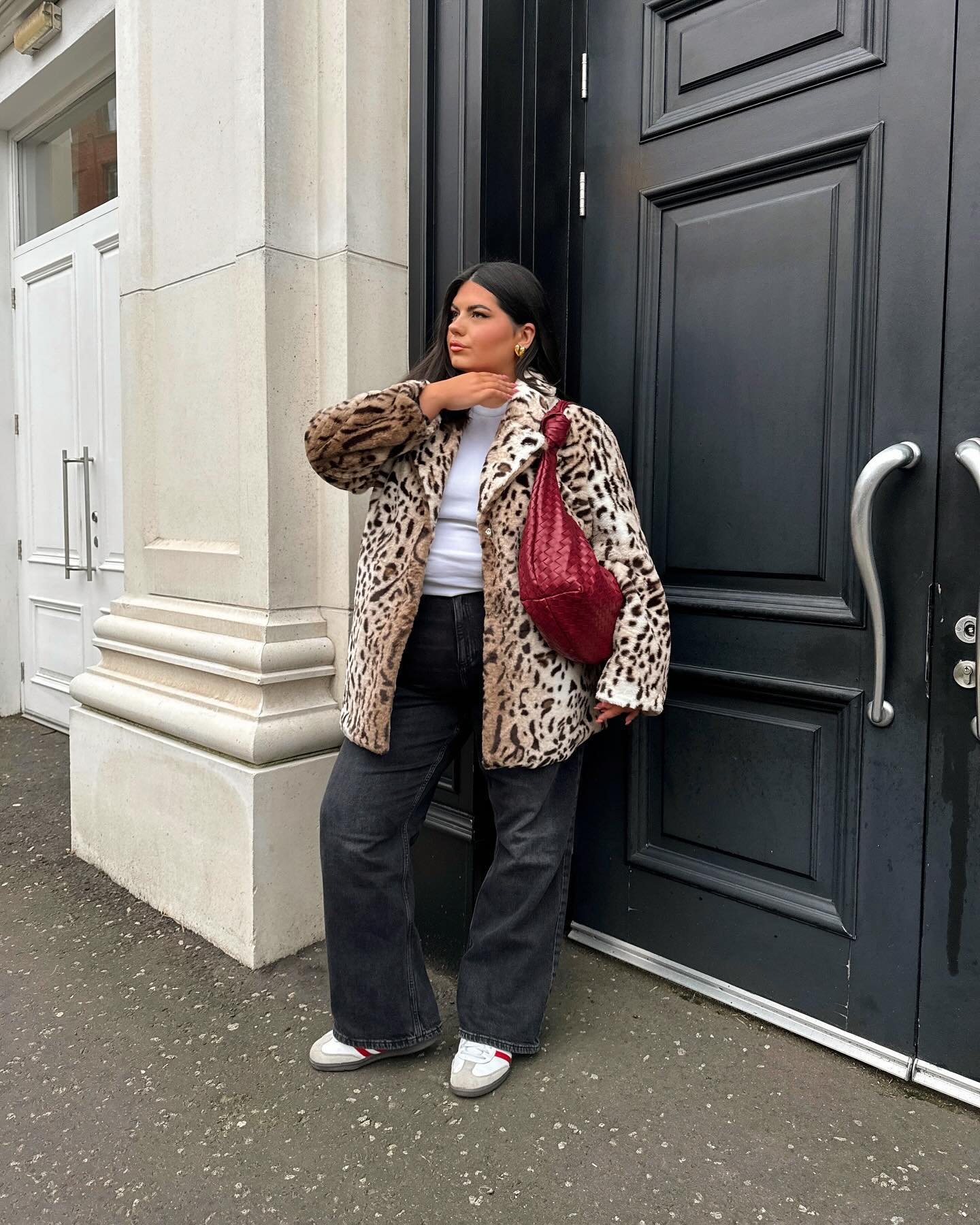 Pessoa com casaco de pelo animal print, jeans escuro e bolsa vermelha. Ideias de looks de frio.