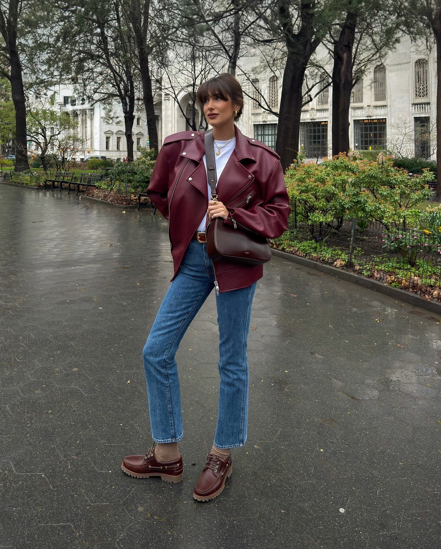 Casaco vinho, jeans e botas em parque urbano, look de frio casual e elegante.