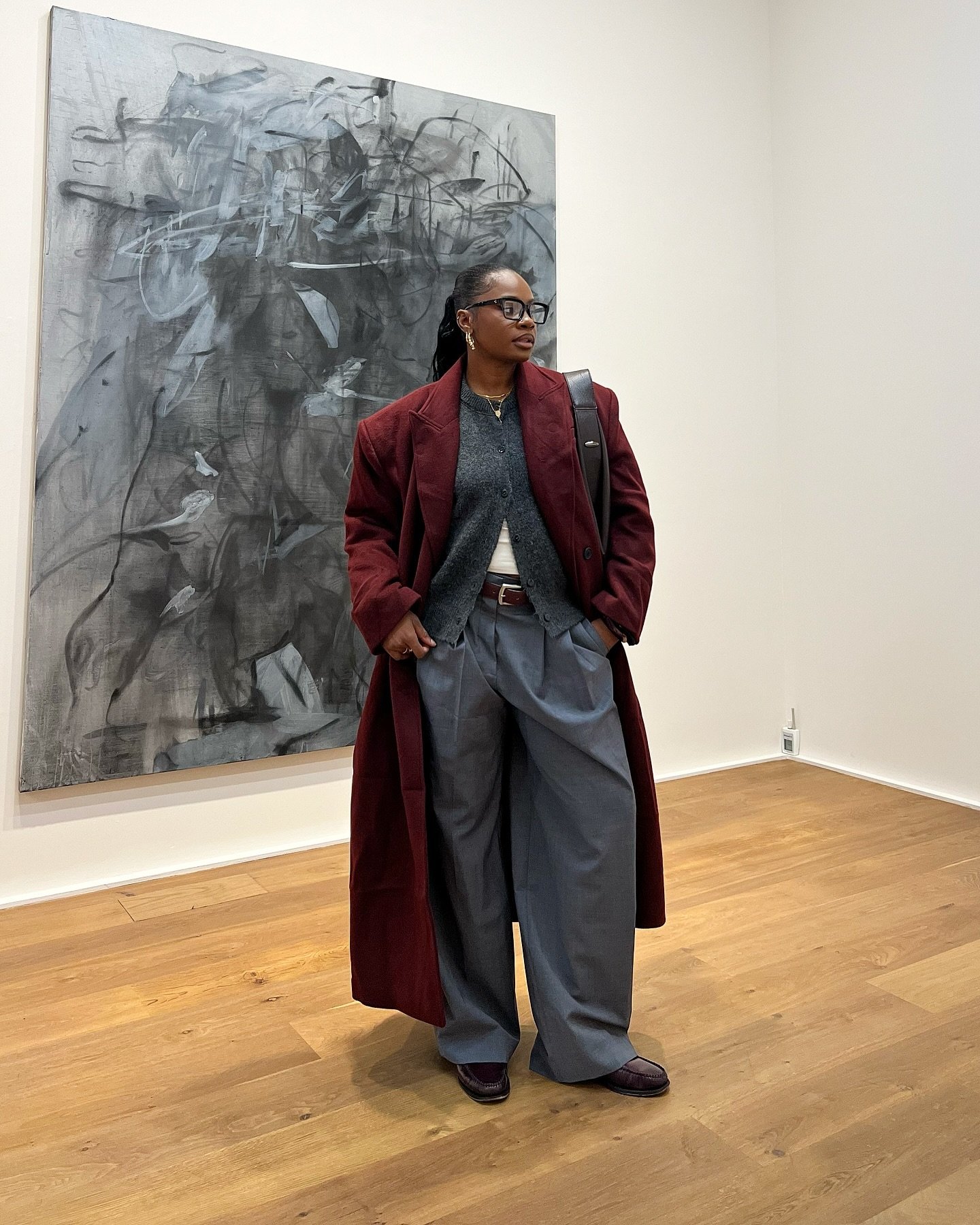 Casaco vinho sobre roupa cinza e calça larga em galeria de arte, exemplificando ideias de looks de frio.