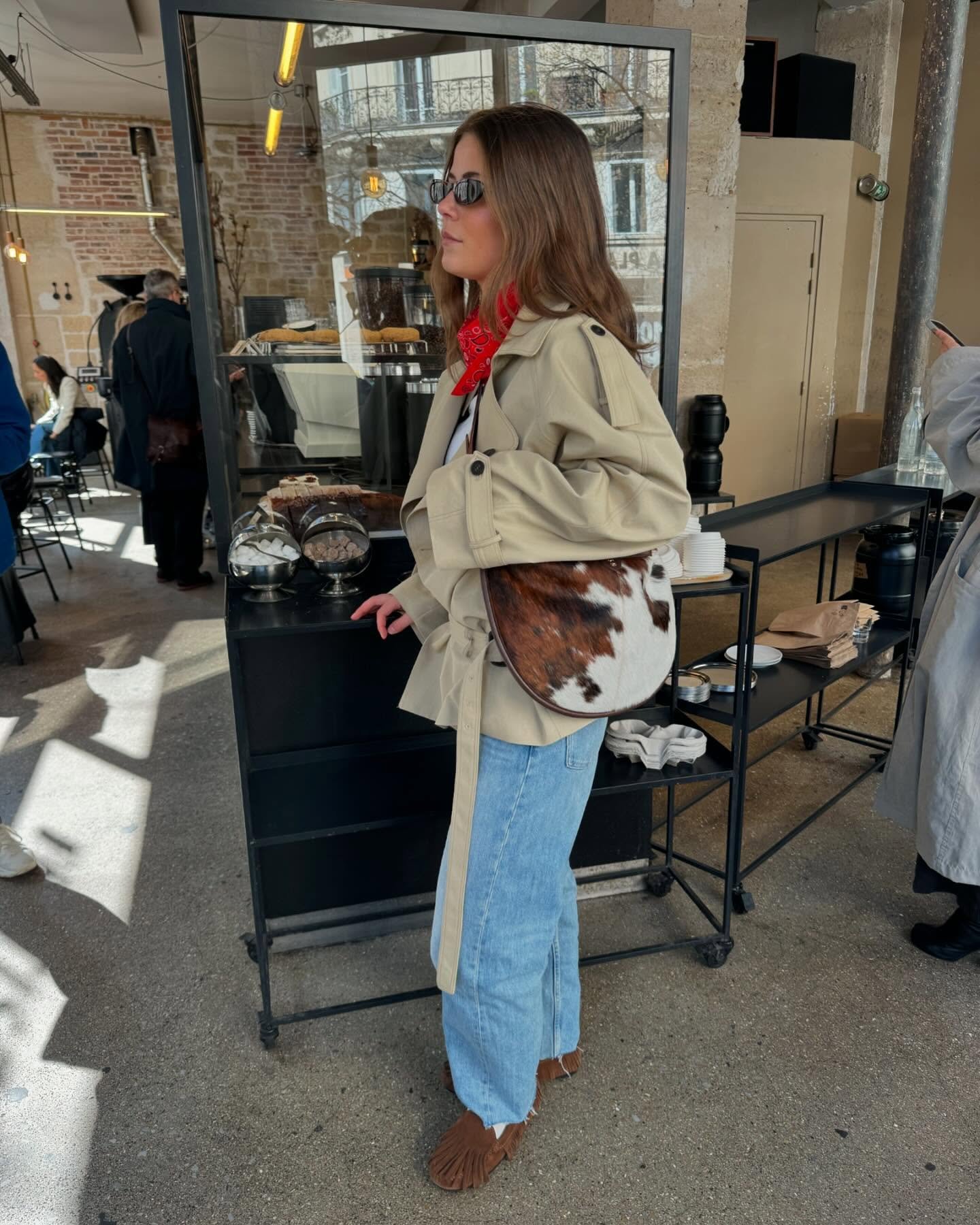 Pessoa com trench coat bege, calça jeans e botas, em um café, inspira ideias de looks de frio.