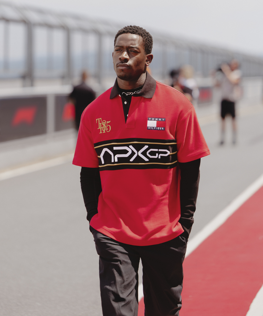 Homem em camisa vermelha caminha em pista de corrida, evocando cena de filme F1.