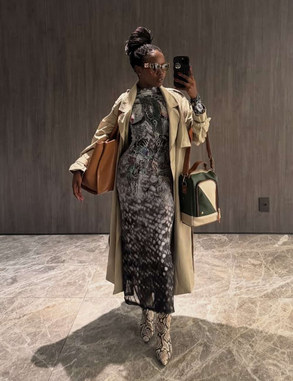 Pessoa vestindo sobretudo e vestido estampado, com bolsa elegante em ambiente interno, segura lancheiras estilosas.