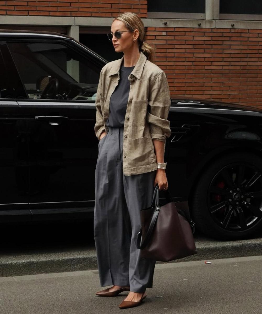 Mulher elegante usando alfaiataria, combinando uma jaqueta bege com calça cinza larga, carregando bolsa marrom.