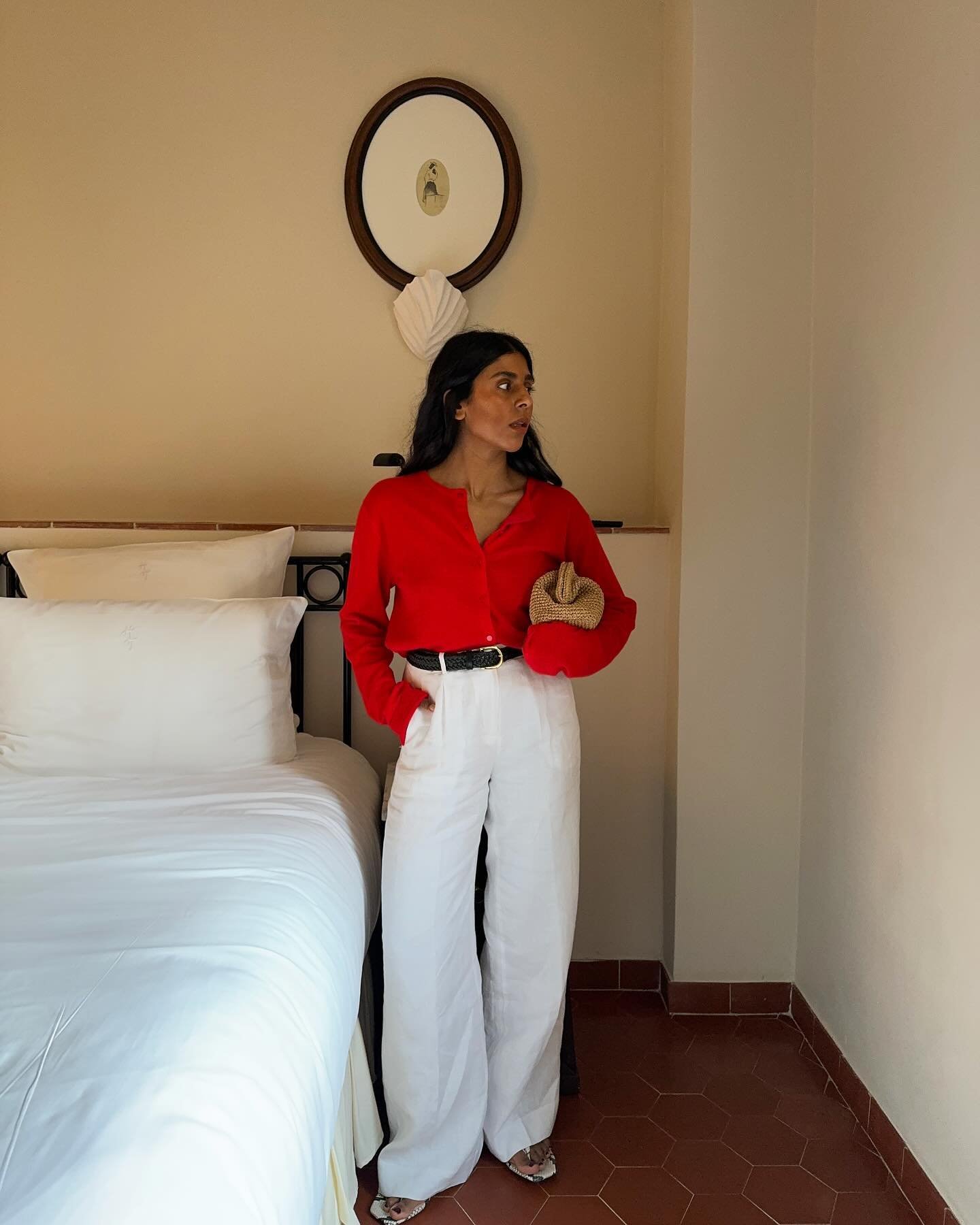 Pessoa em um quarto, veste blusa vermelha e calça branca, segurando uma bolsa. Looks com blusa vermelha