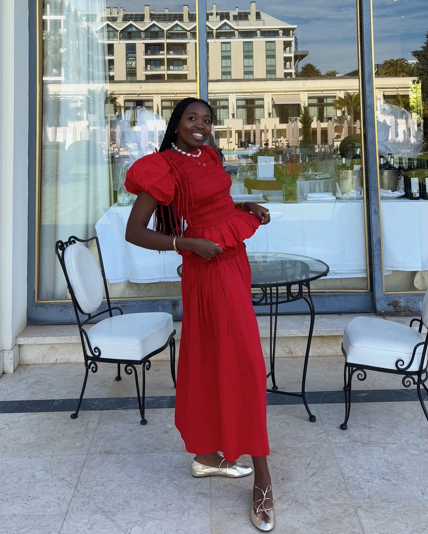 Pessoa sorridente em frente a um prédio, usando conjunto vermelho elegante. Looks com blusa vermelha