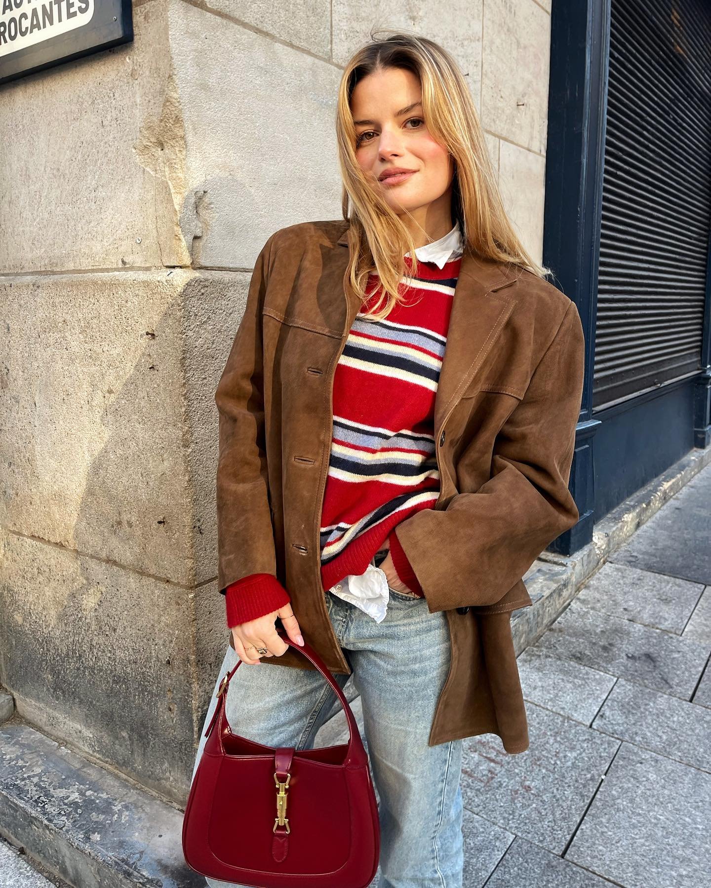 Pessoa com casaco marrom e suéter listrado vermelho, segurando bolsa vermelha na rua. Looks com blusa vermelha