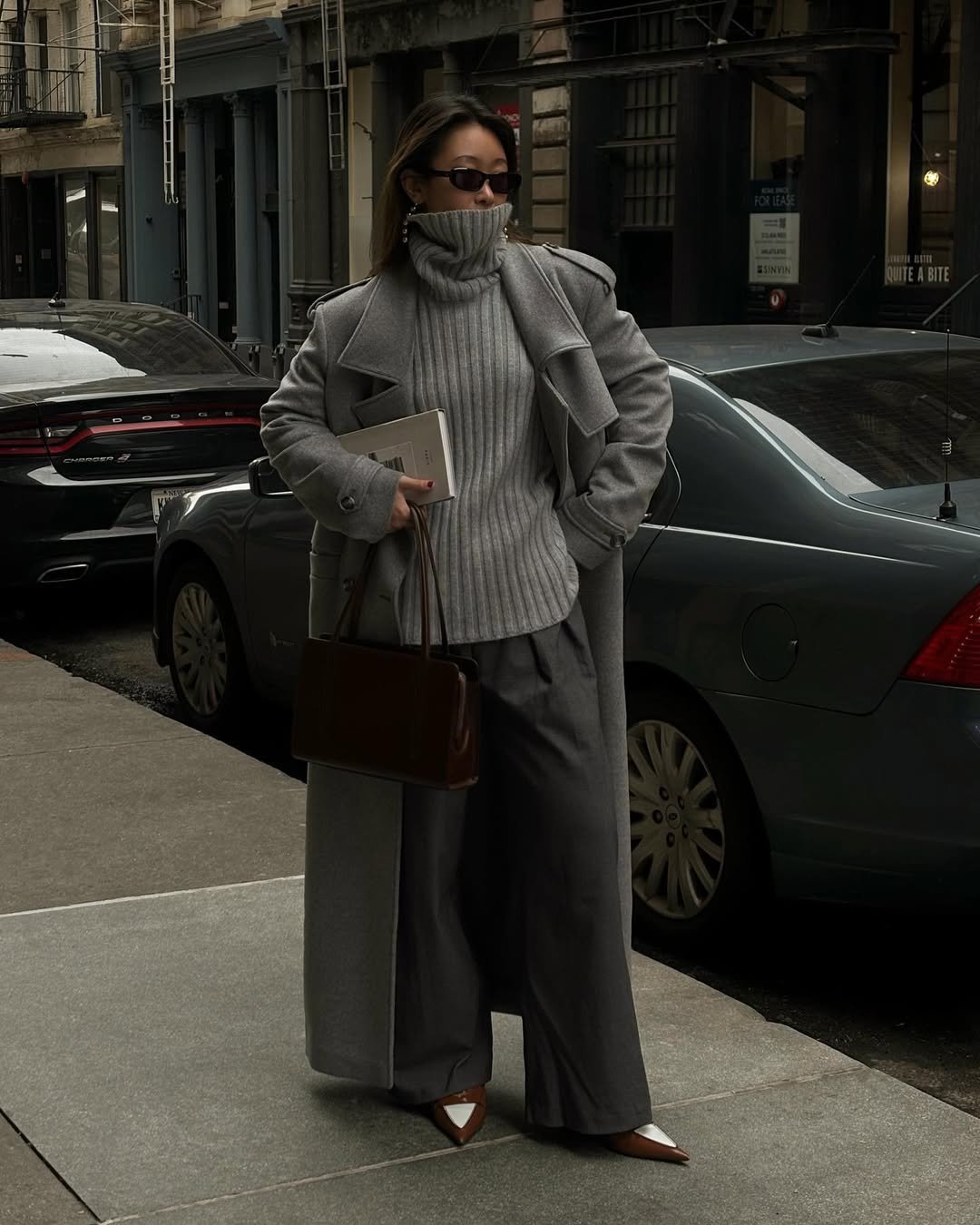 Casaco cinza e gola alta em ambiente urbano, bolsa marrom, criando looks sofisticados de inverno.