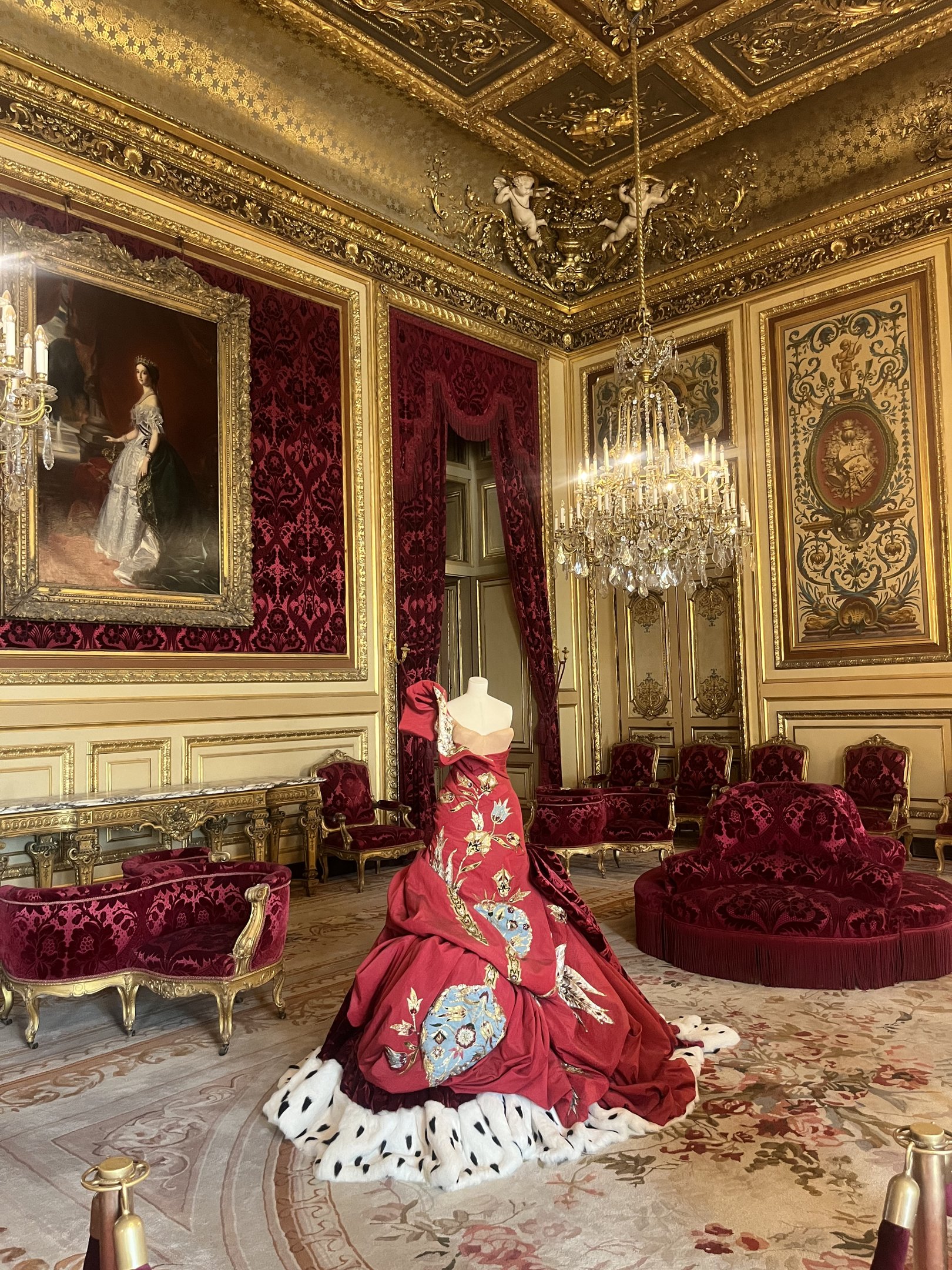 Salão luxuoso com vestido vermelho elaborado em exibição, combinando com a rica decoração do espaço. Couture.