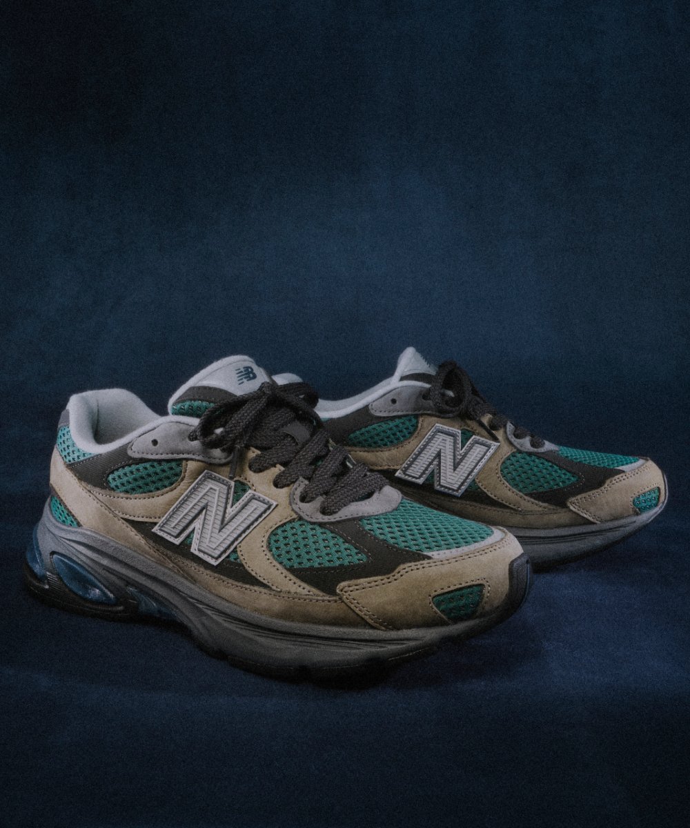 Tênis New Balance verde e bege com tecnologia ABZORB em fundo azul.
