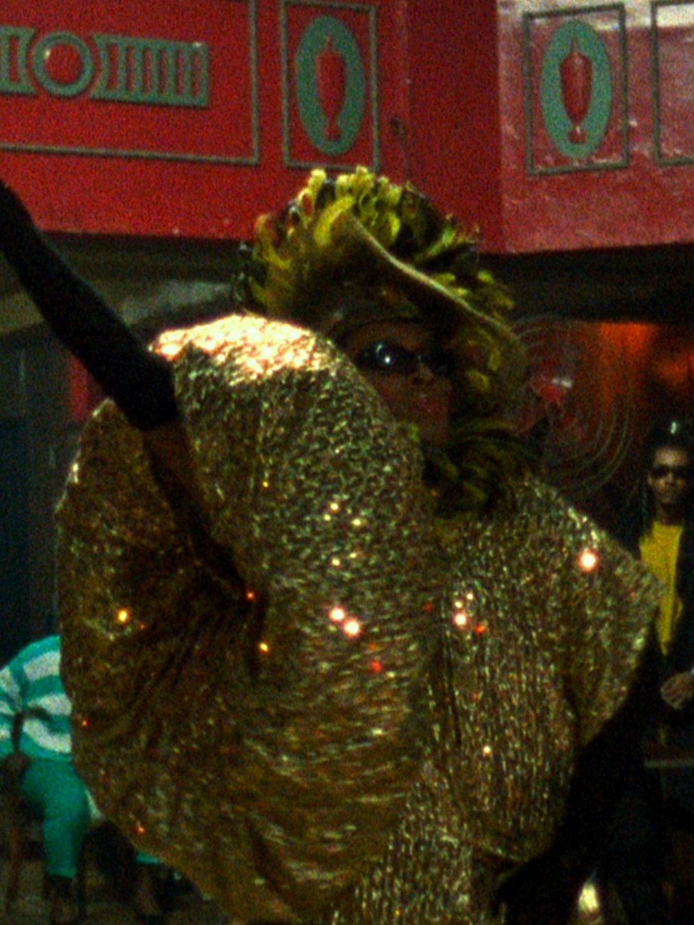 Pessoa em traje dourado e extravagante, com adereços na cabeça, participando de um evento LGBTQIAPN+.