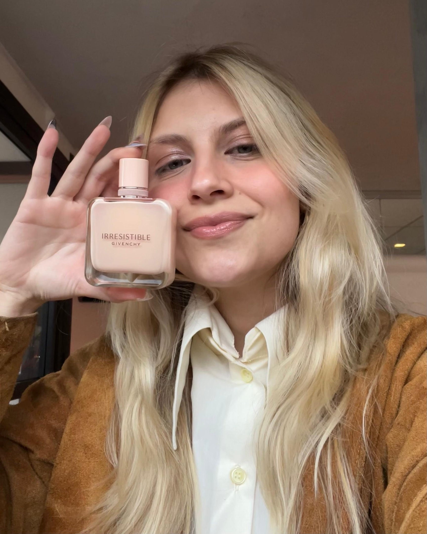 Pessoa segurando frasco de perfume Givenchy, ideal para o inverno, com expressão satisfeita.