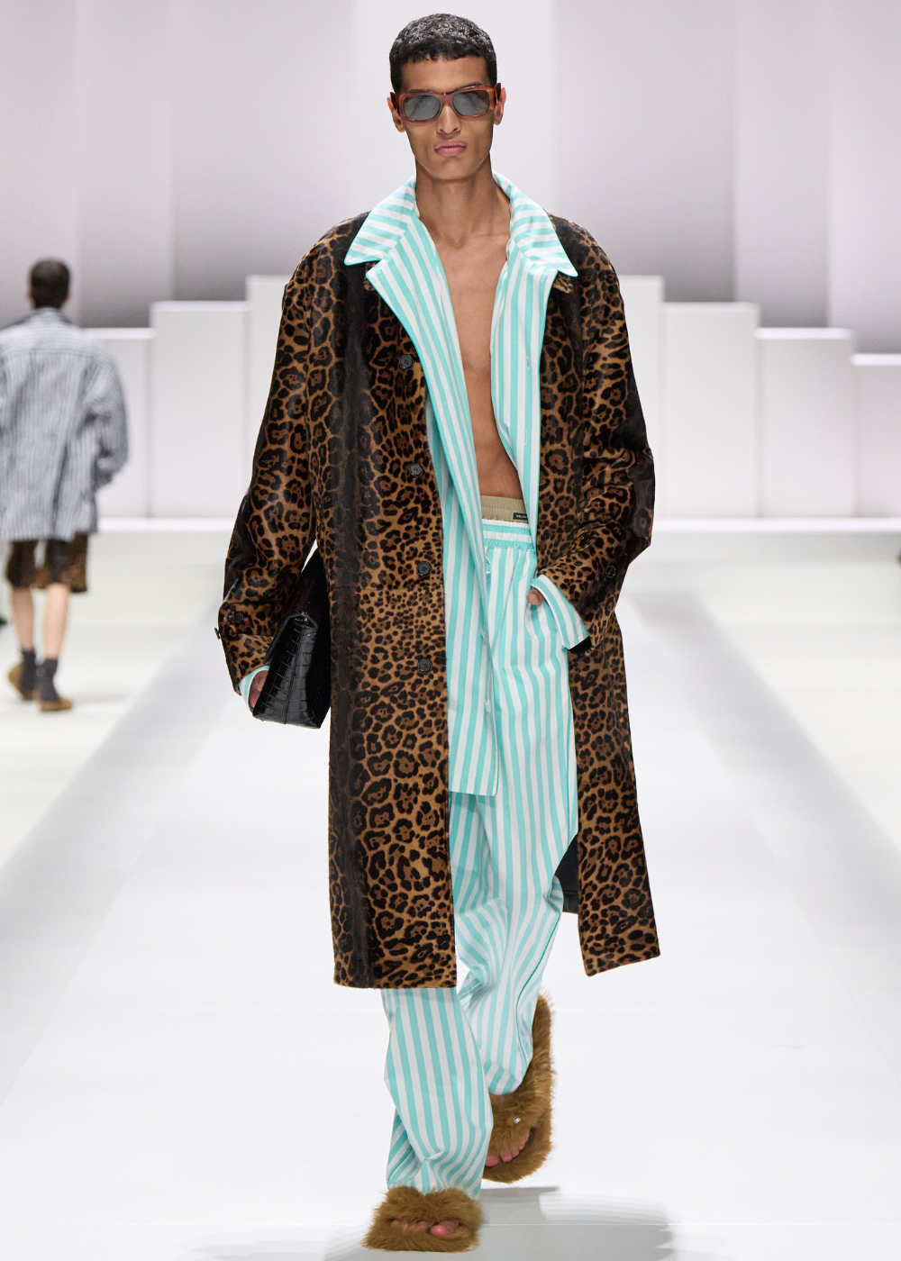 Modelo em passarela vestindo sobretudo de estampa animal e look listrado tipo pijama azul claro.