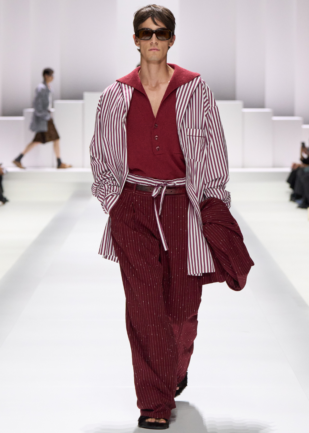 Modelo desfilando com roupa estilo pijama em vermelho e branco, combinando camiseta e calça listrada.