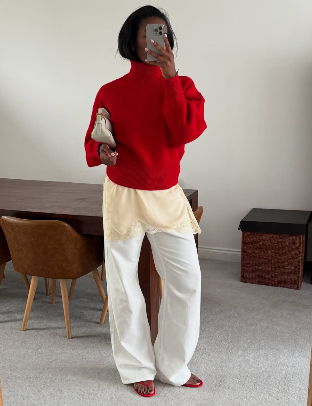 Uma pessoa vestindo suéter vermelho e calça clara segura um celular no espelho.